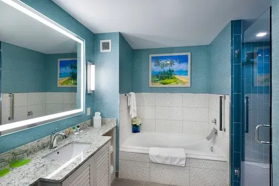 A bathroom with blue walls, white bathtub, vanity, and a large mirror with bright lighting.