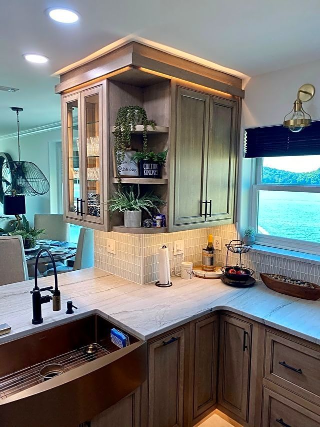 Kitchen with light wood cabinets, corner display shelves with plants, and a copper sink.