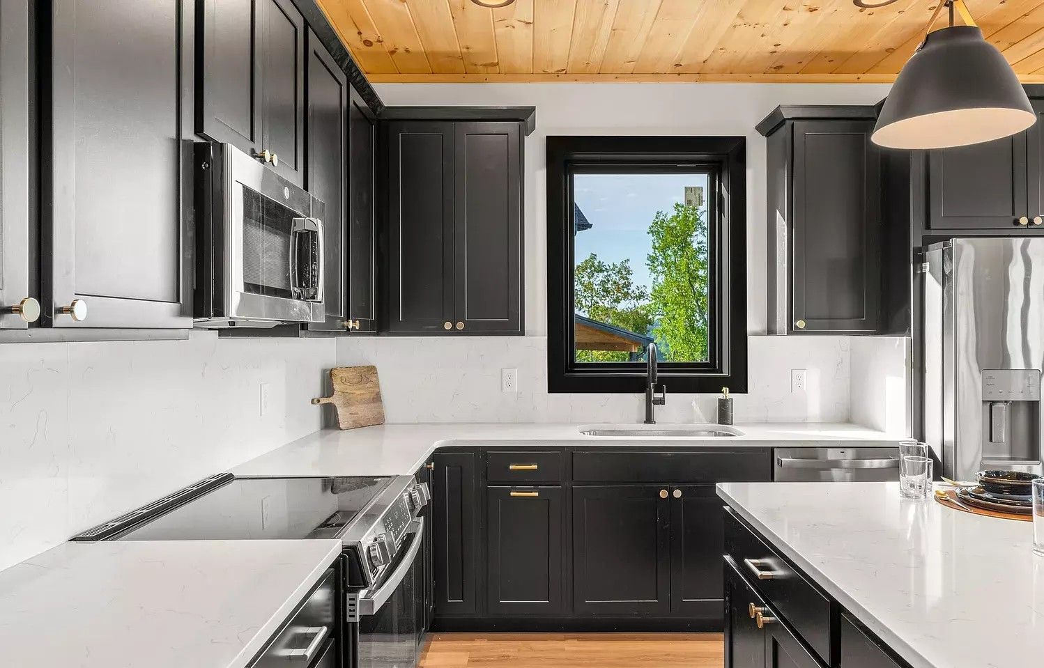 Modern kitchen with dark cabinets, white countertops, and a window above the sink