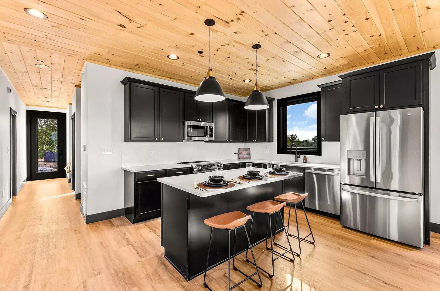 Modern kitchen with black cabinets, stainless steel appliances, island seating, and wood ceiling