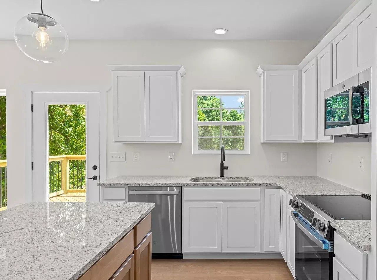 Bright white kitchen with granite counters, white cabinets, stainless stove, and a window over the sink.