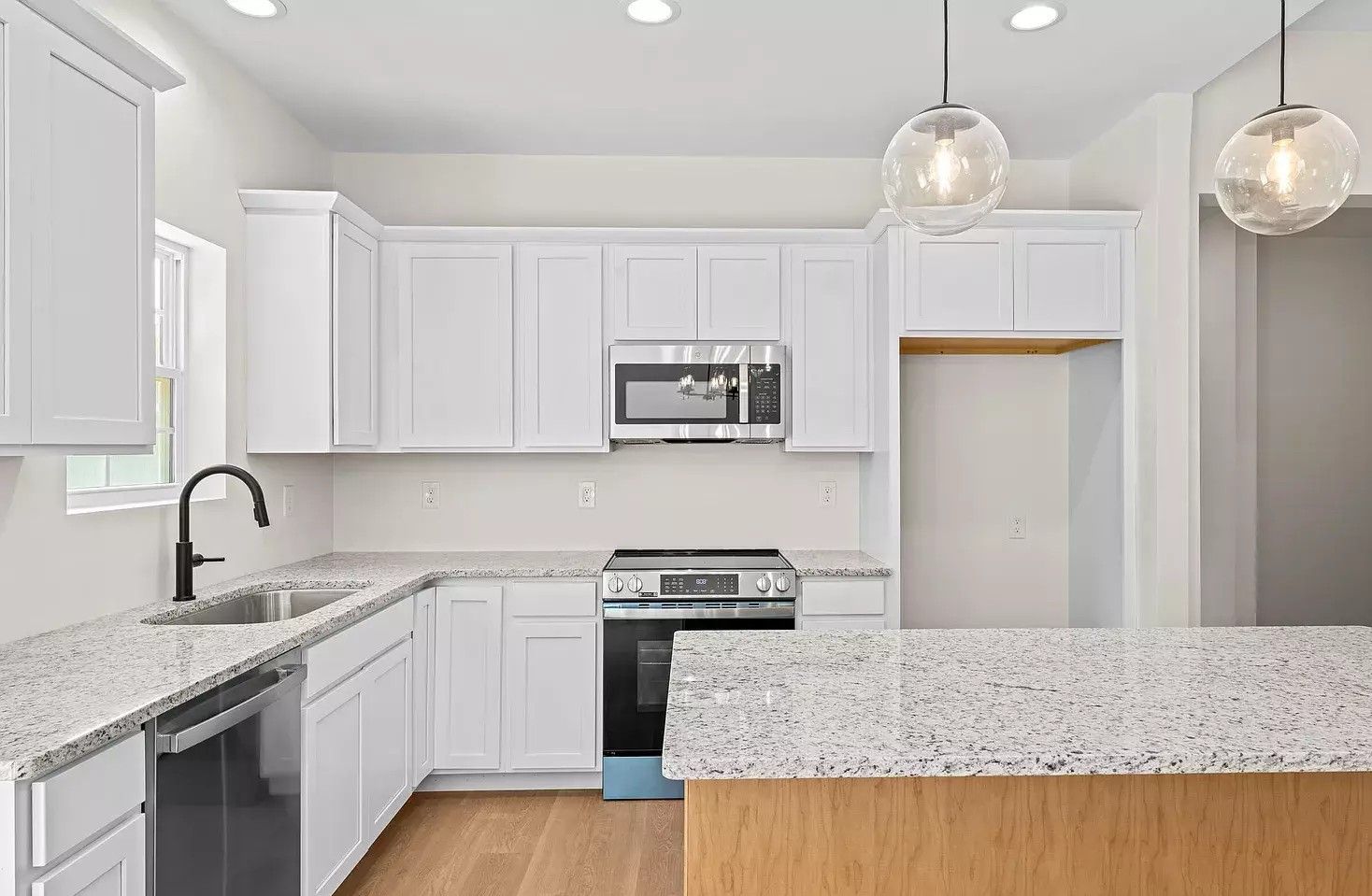 Bright white kitchen with granite counters, stainless appliances, and pendant lights