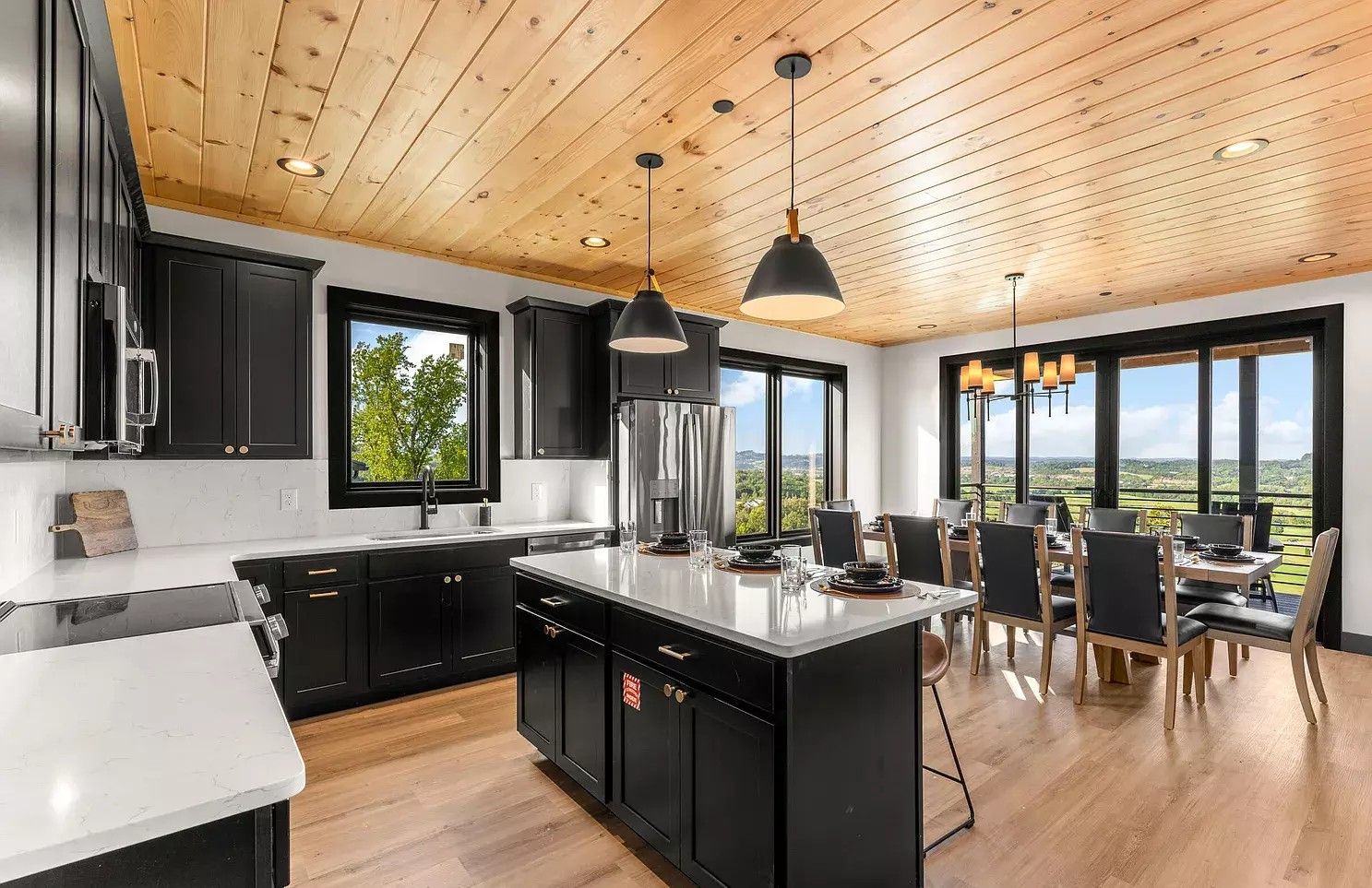 Modern kitchen with black cabinets, wood ceiling, island, and large windows overlooking a view