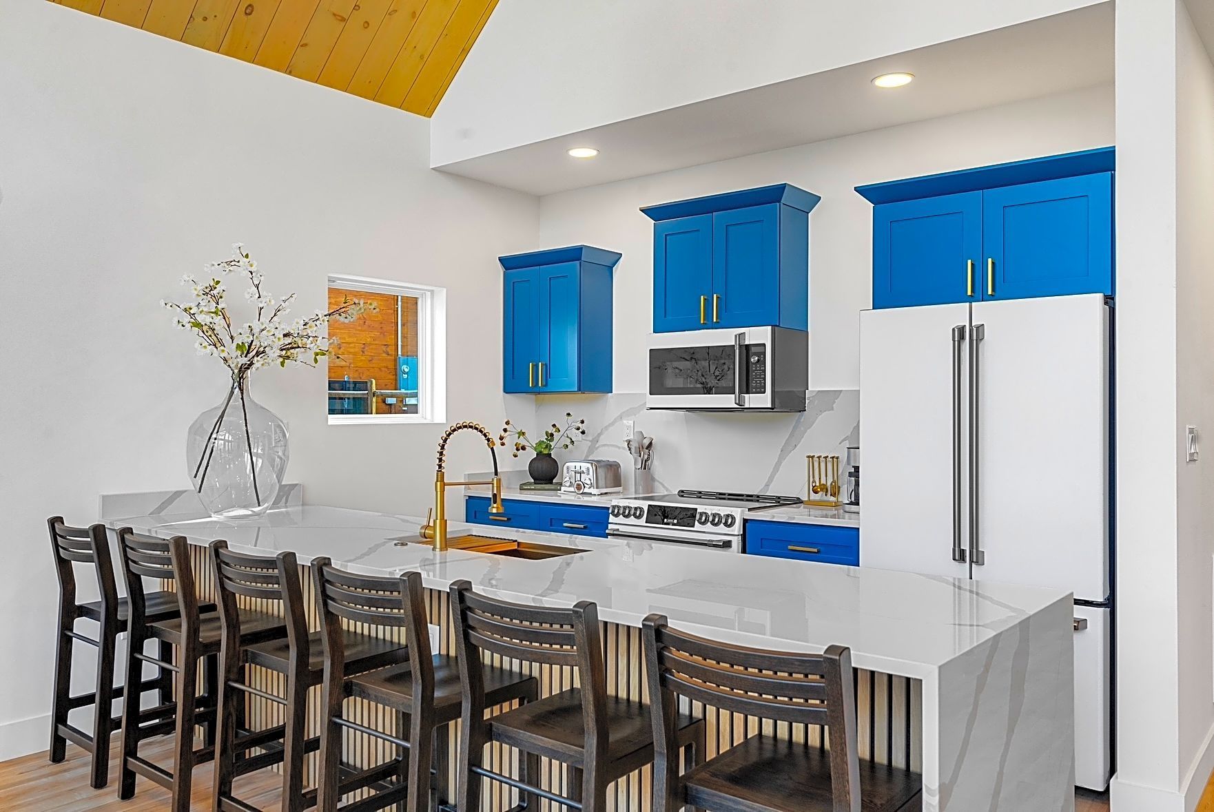 Bright blue kitchen cabinets with a white countertop and gold fixtures. Black bar stools line the island.