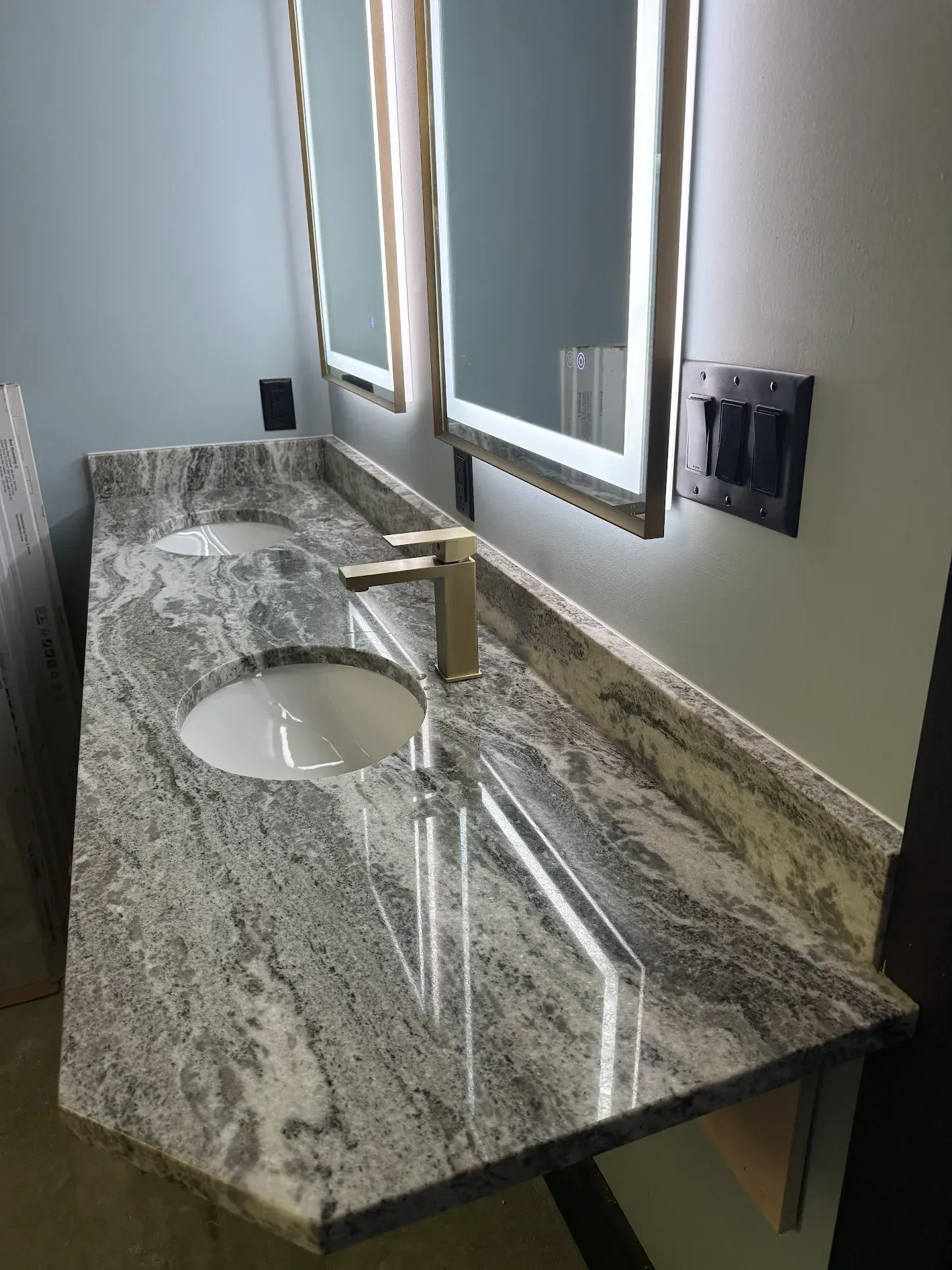 Double sink vanity with gray granite countertop and lighted mirrors.