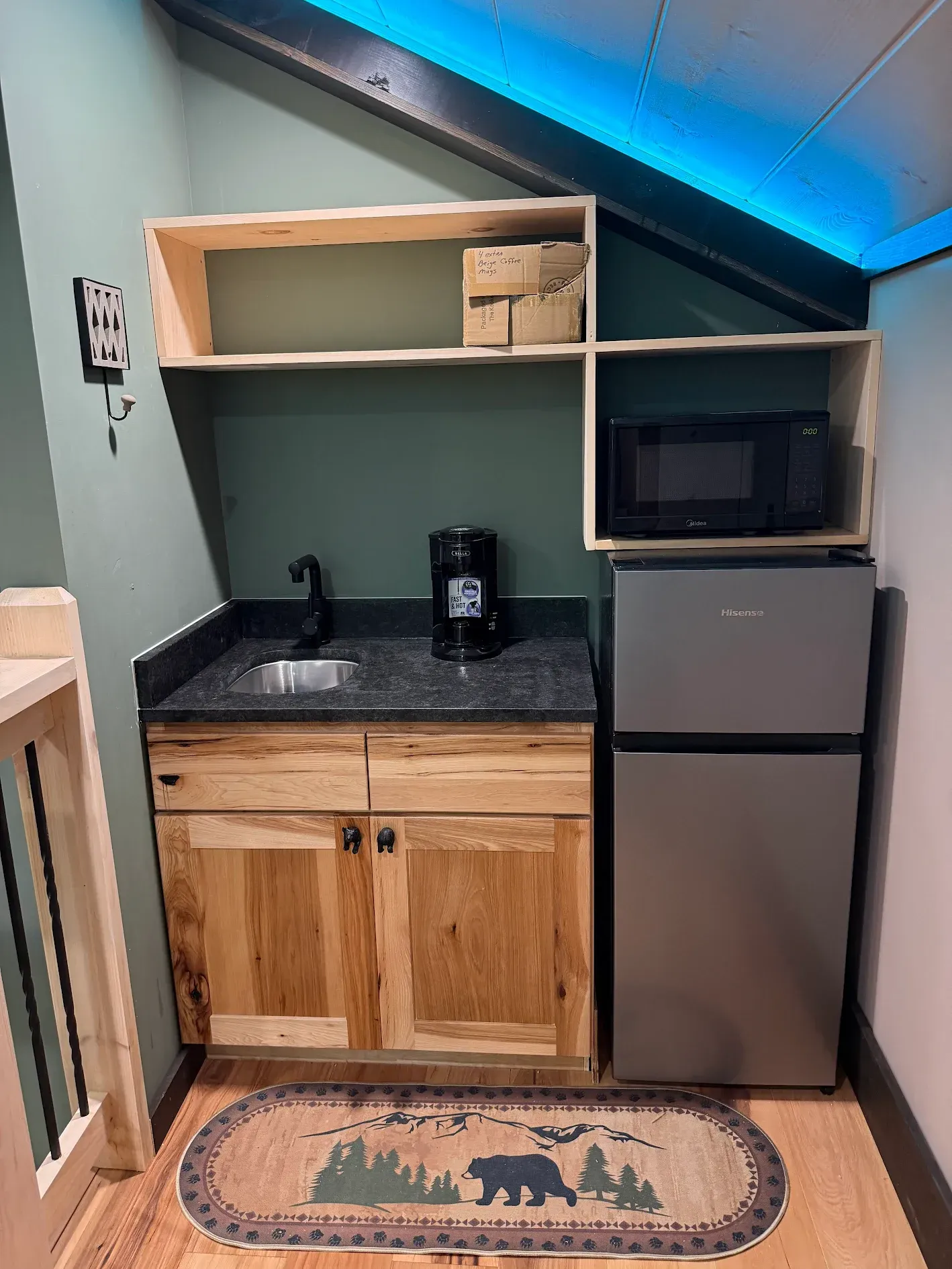 Small kitchenette with sink, microwave, mini-fridge, and shelving in a cabin setting.