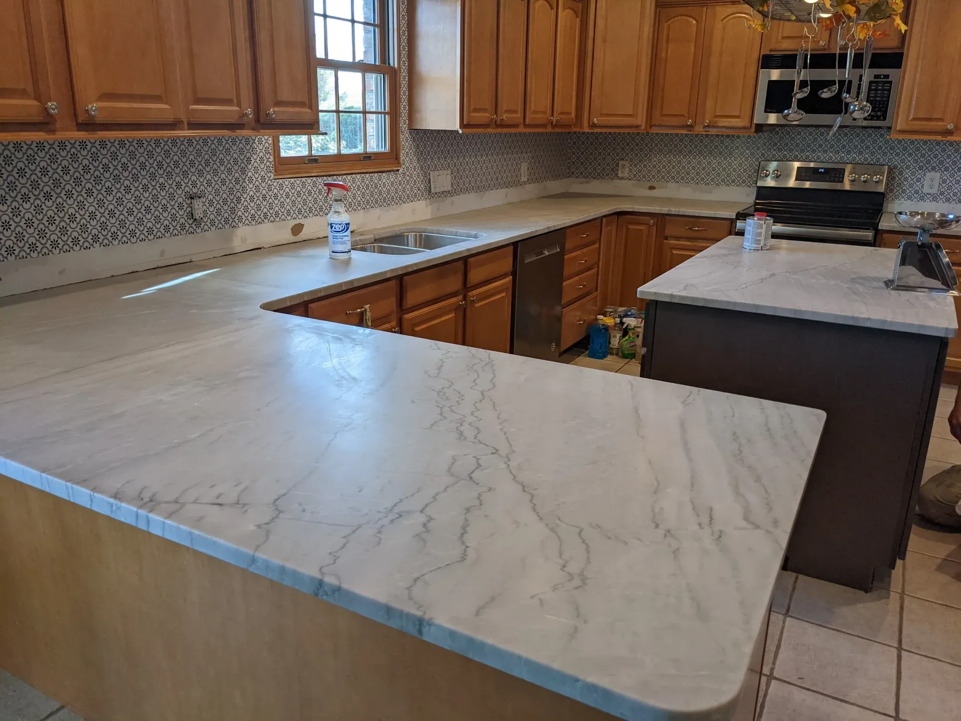 Kitchen with light countertops, wooden cabinets, and a multi-colored backsplash.