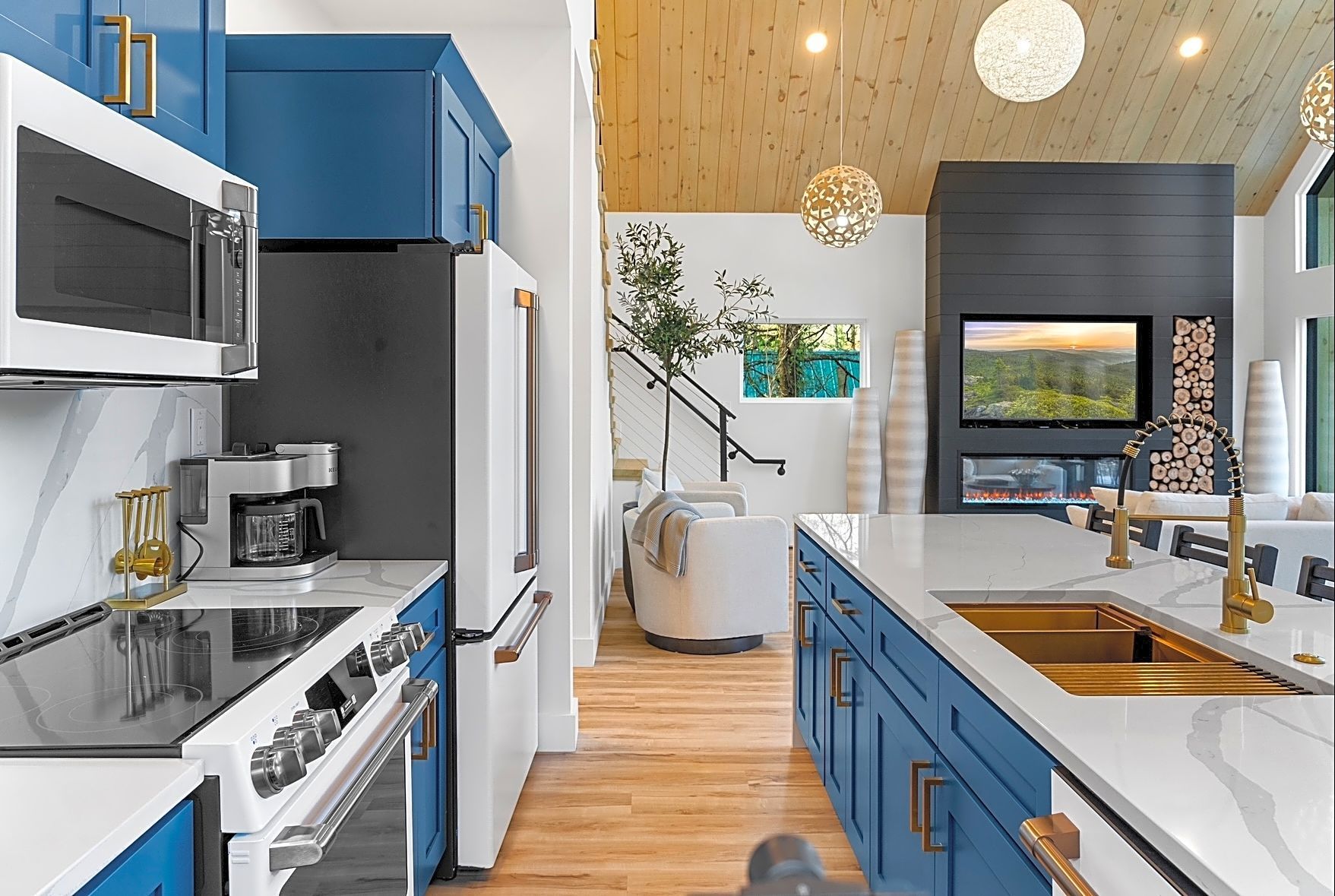Blue kitchen with white countertops and gold hardware; open to living area with fireplace and wood ceiling.