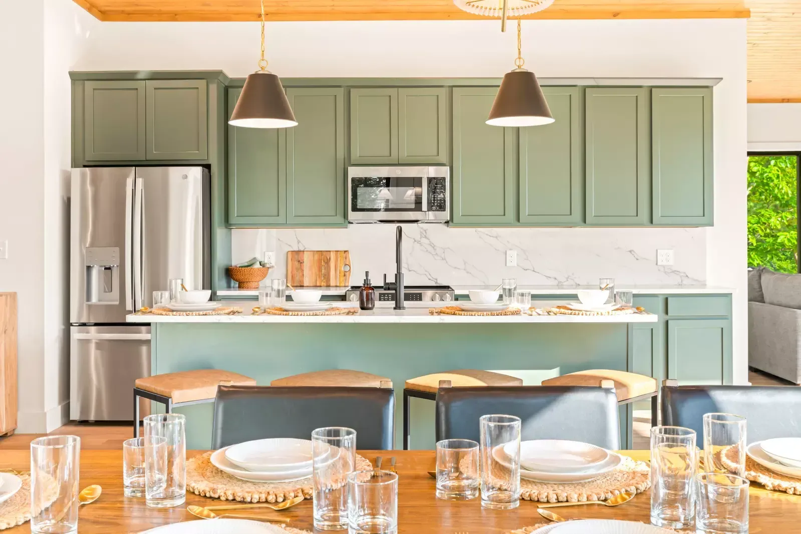 Bright modern kitchen with sage green cabinets, stainless fridge, island, and two pendant lights