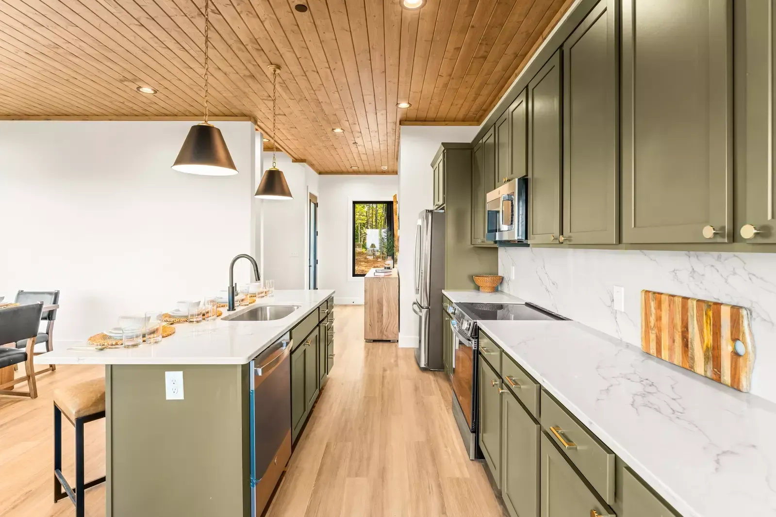 Modern kitchen with green cabinets, white countertops, wood ceiling, and island under pendant lights