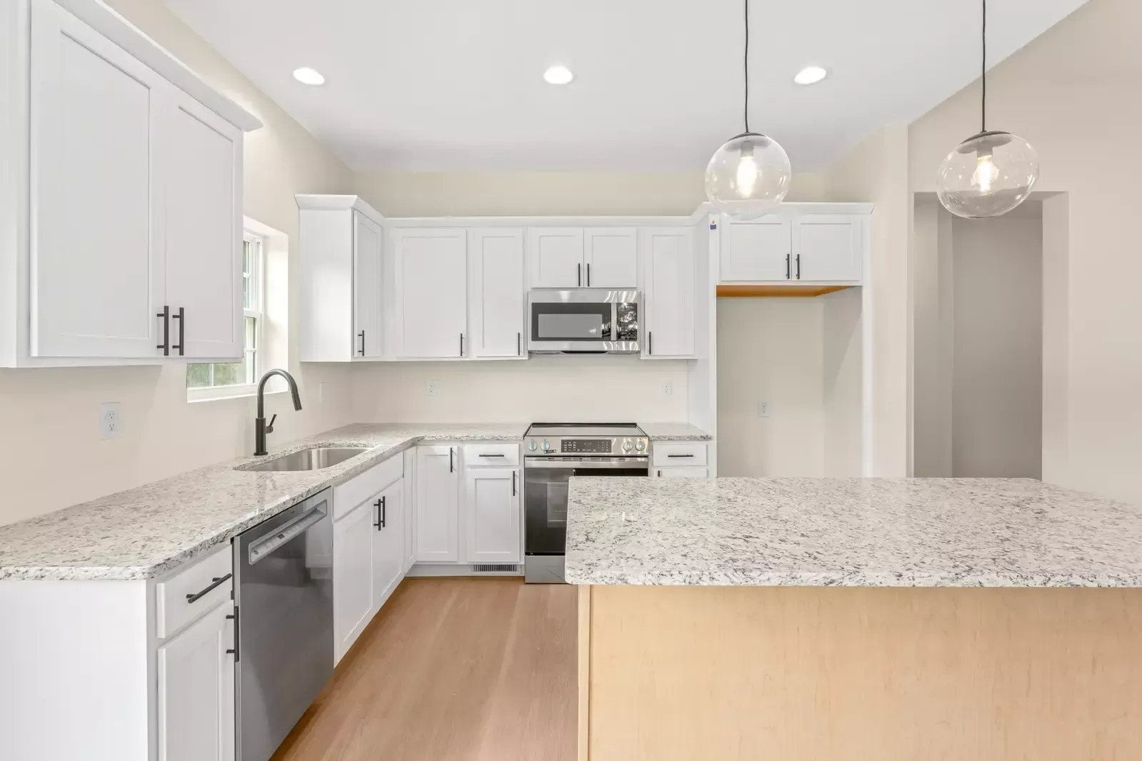Bright modern kitchen with white cabinets, stainless appliances, granite counters, and wood floors