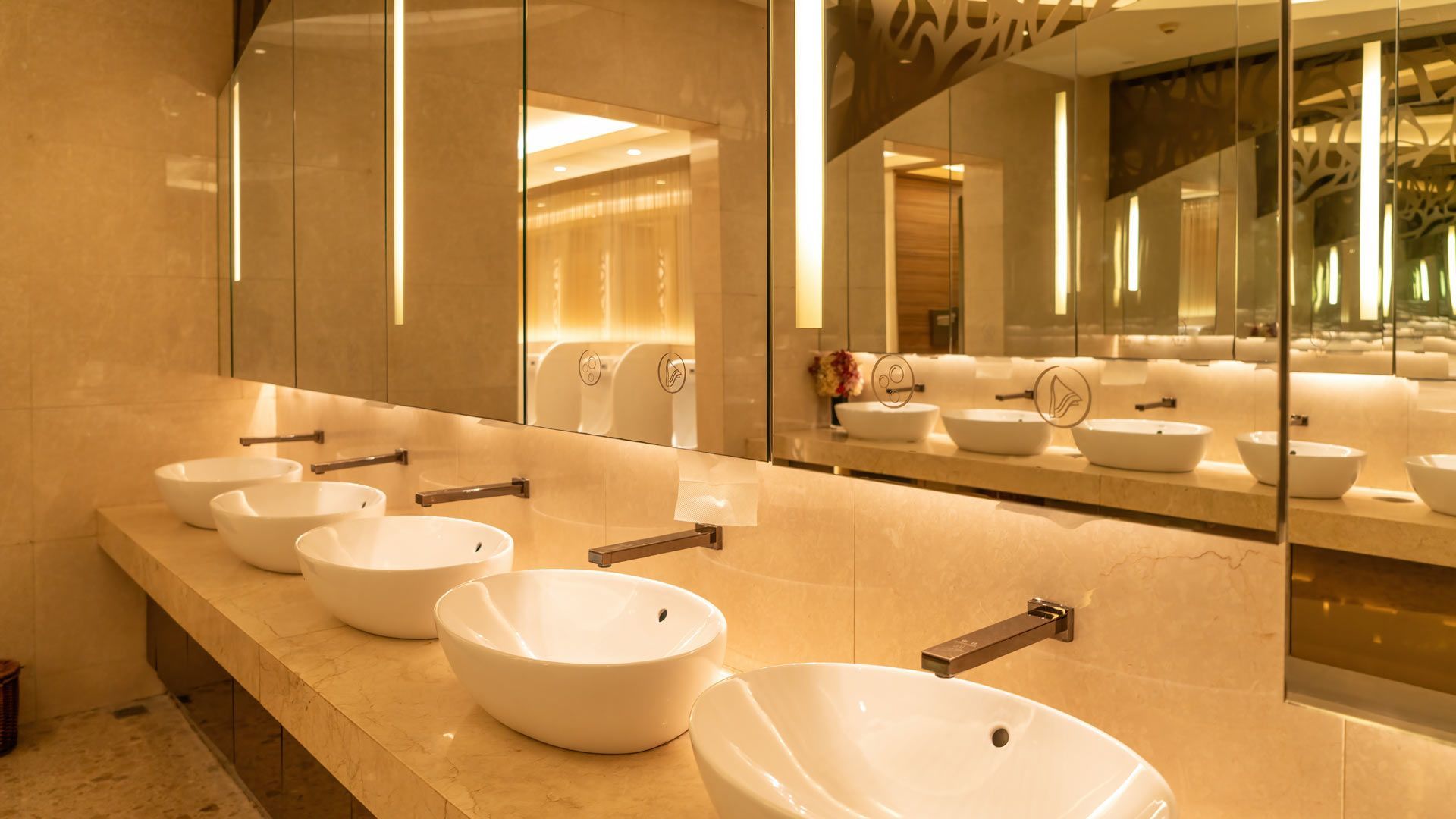Warm-lit modern restroom with rows of white sink basins and wall mirrors
