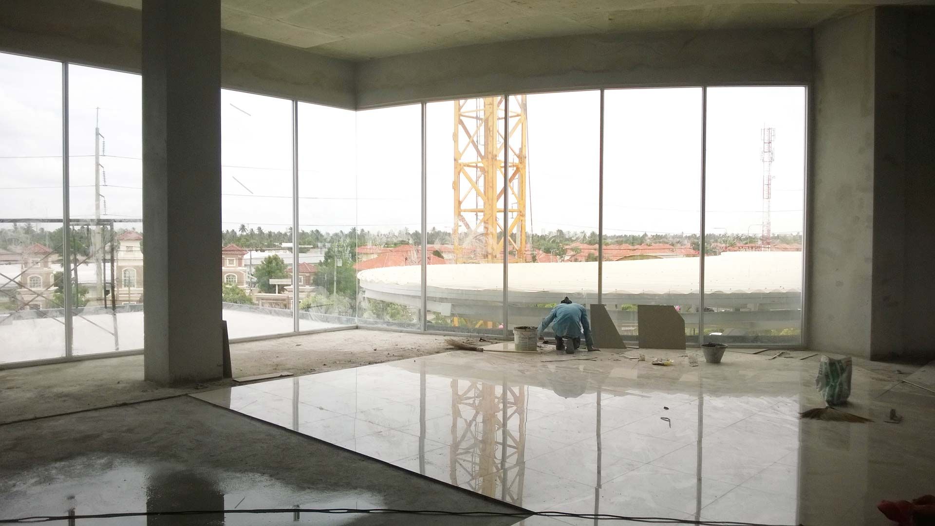 Partially constructed concrete interior with open windows, wet floor reflections, and a yellow crane visible outside