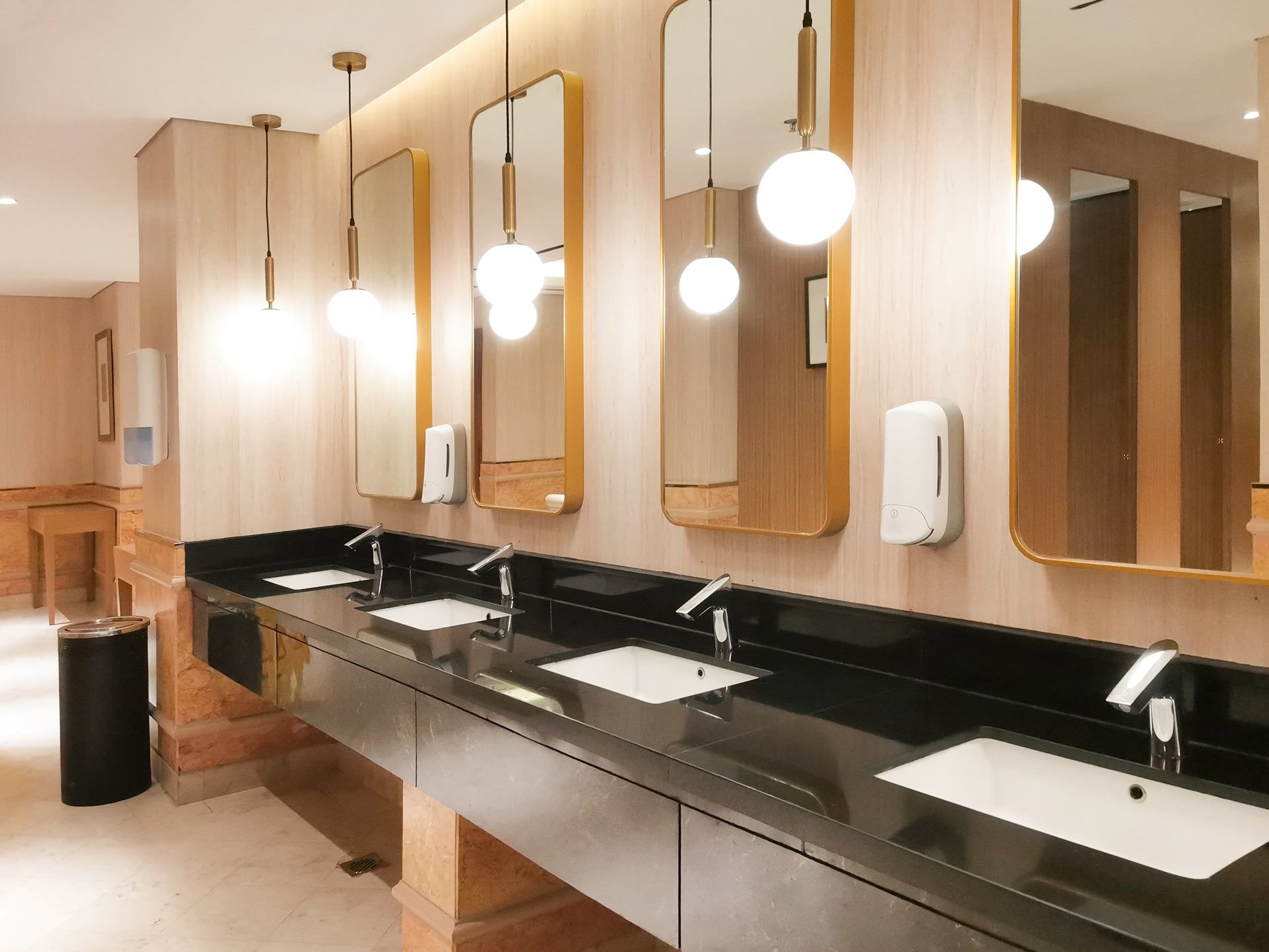 Modern restroom with long black countertop, white sinks, mirrors, and warm pendant lights