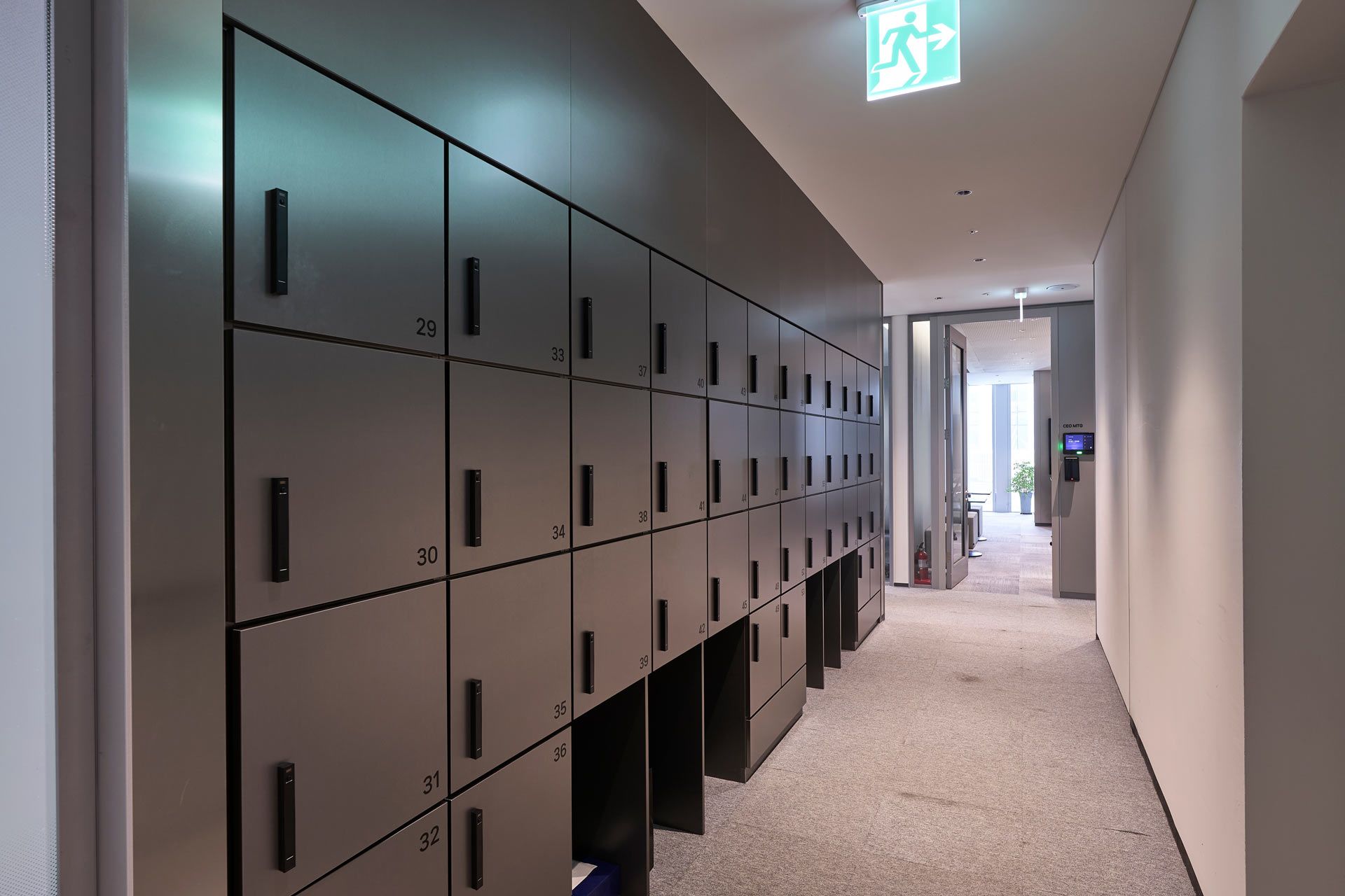 Modern office hallway with wall of black lockers and a lit exit sign