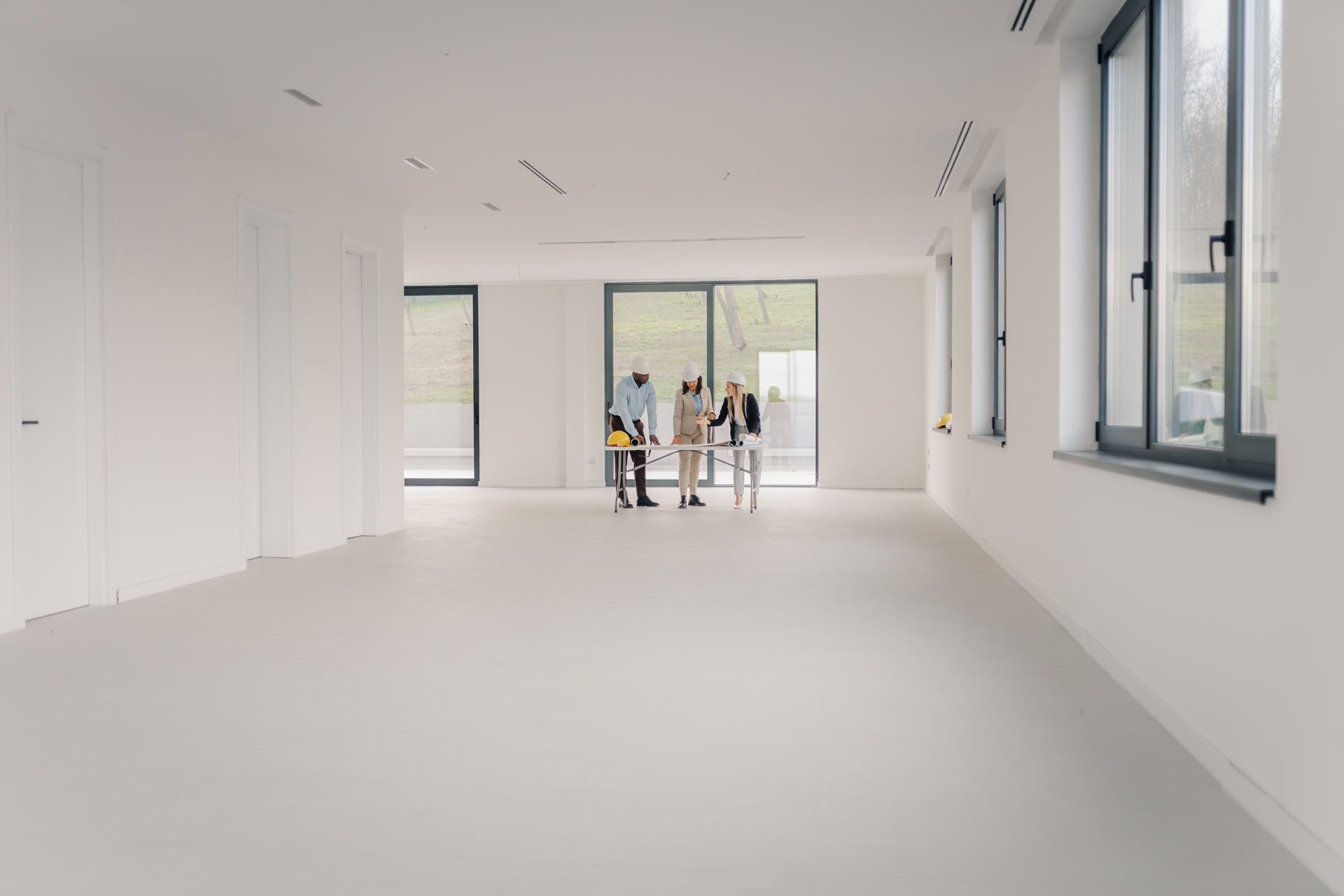 Bright empty white room with large windows and two people standing near the far glass doors