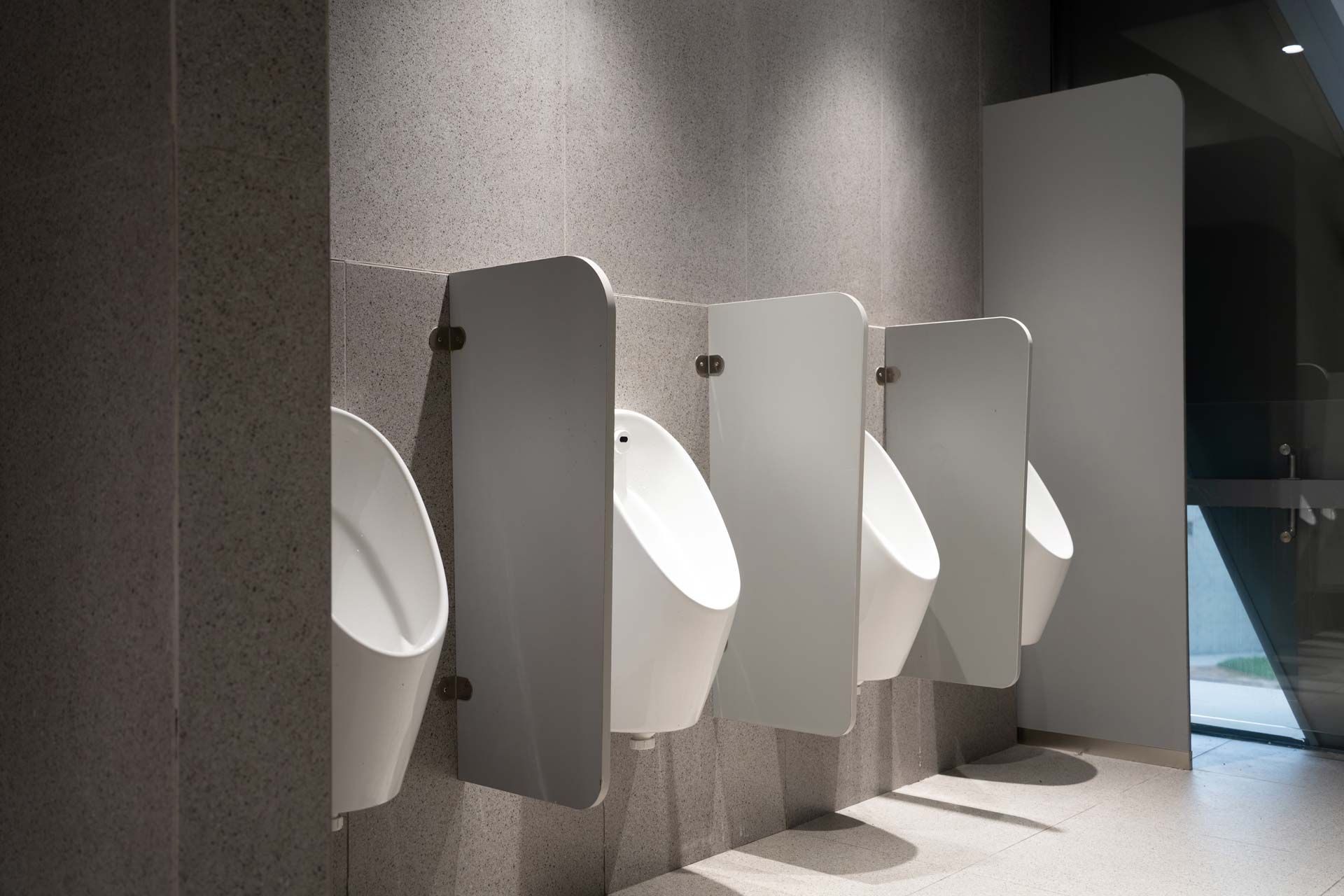 Row of white urinals in a modern public restroom with gray stall dividers.