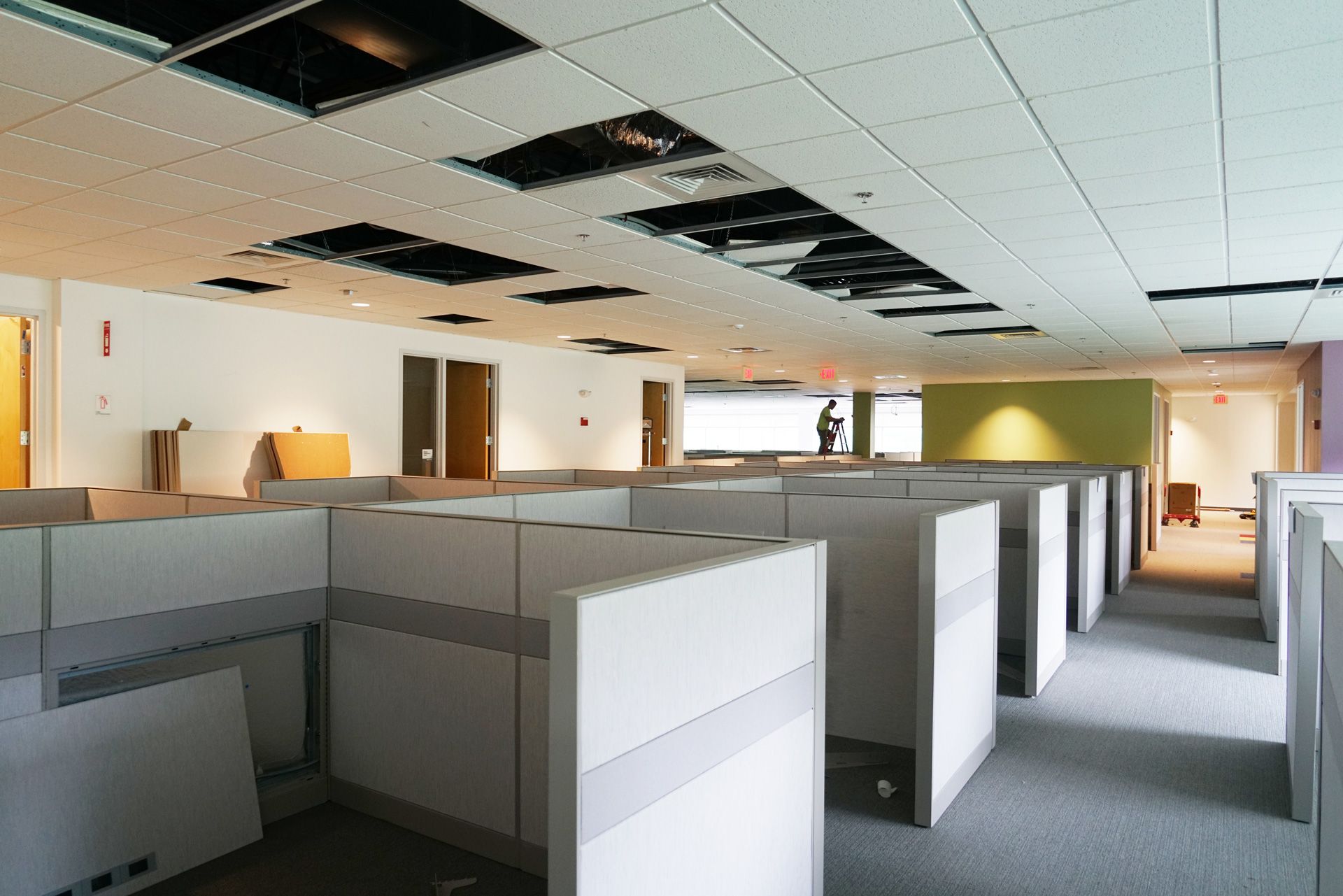 Empty office cubicles in a bright, modern workspace with overhead ceiling panels missing