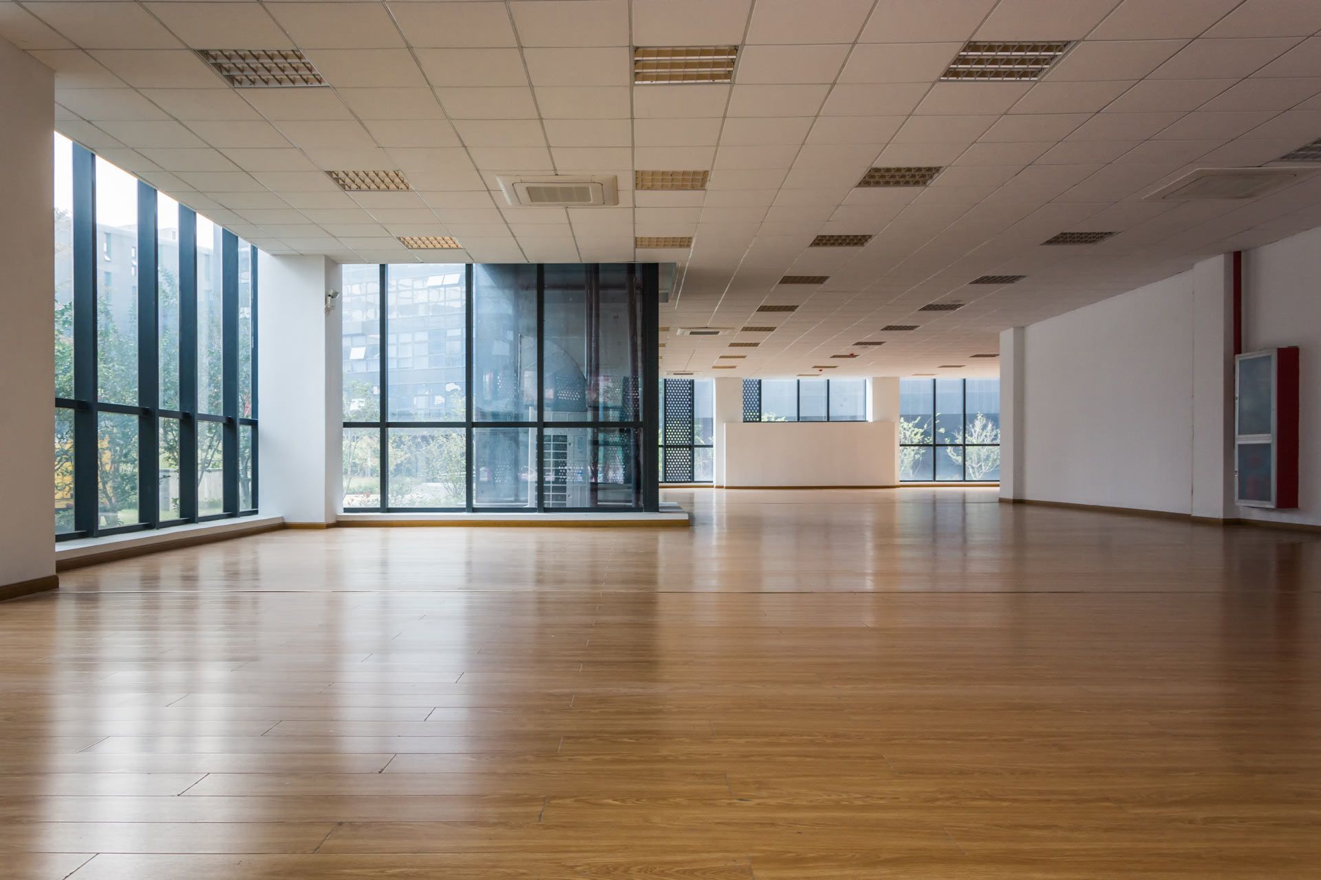 Empty modern room with wood floor, large windows, and white ceiling panels.