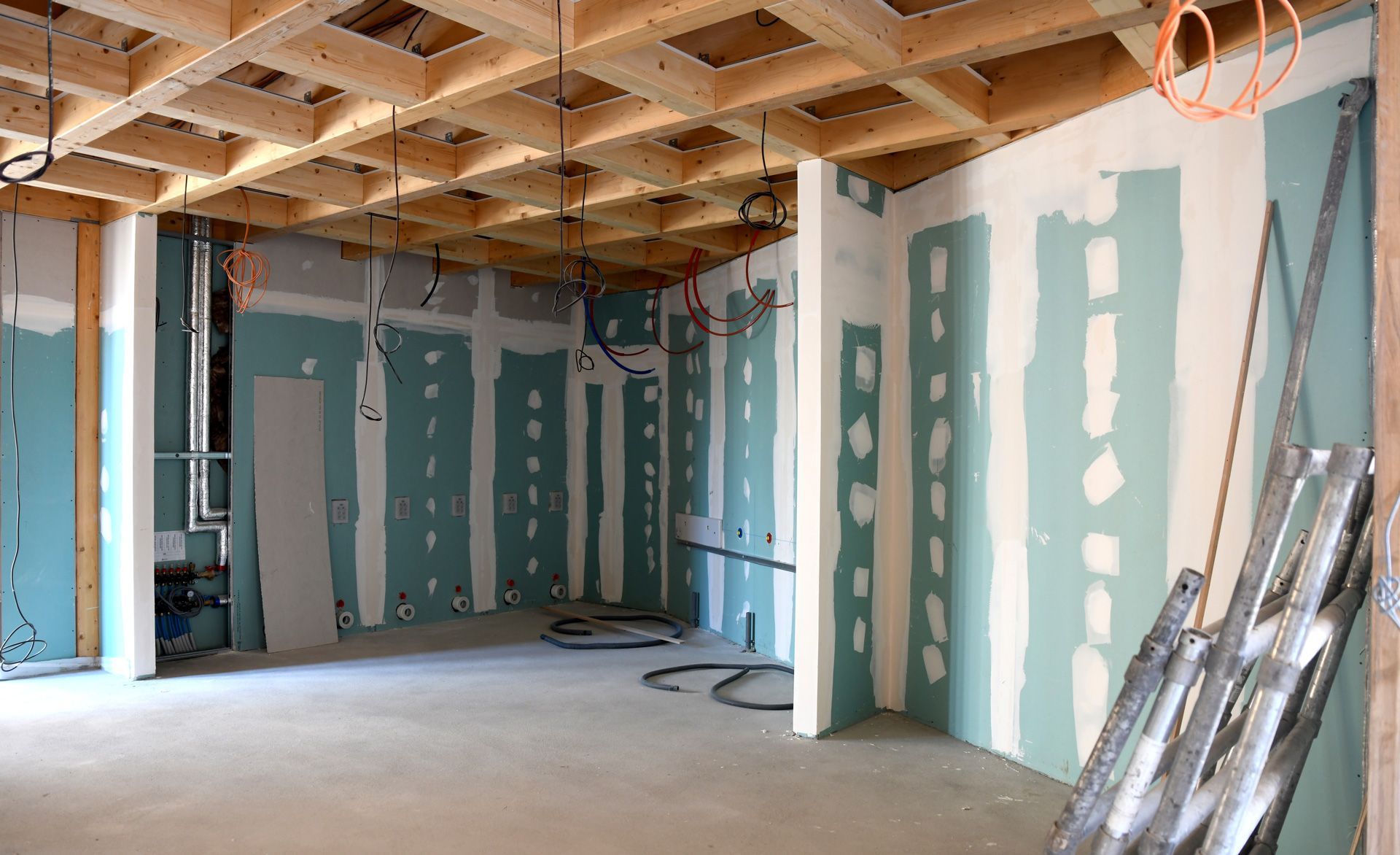 Partially finished room with drywall, exposed ceiling joists, and construction materials leaning against the wall