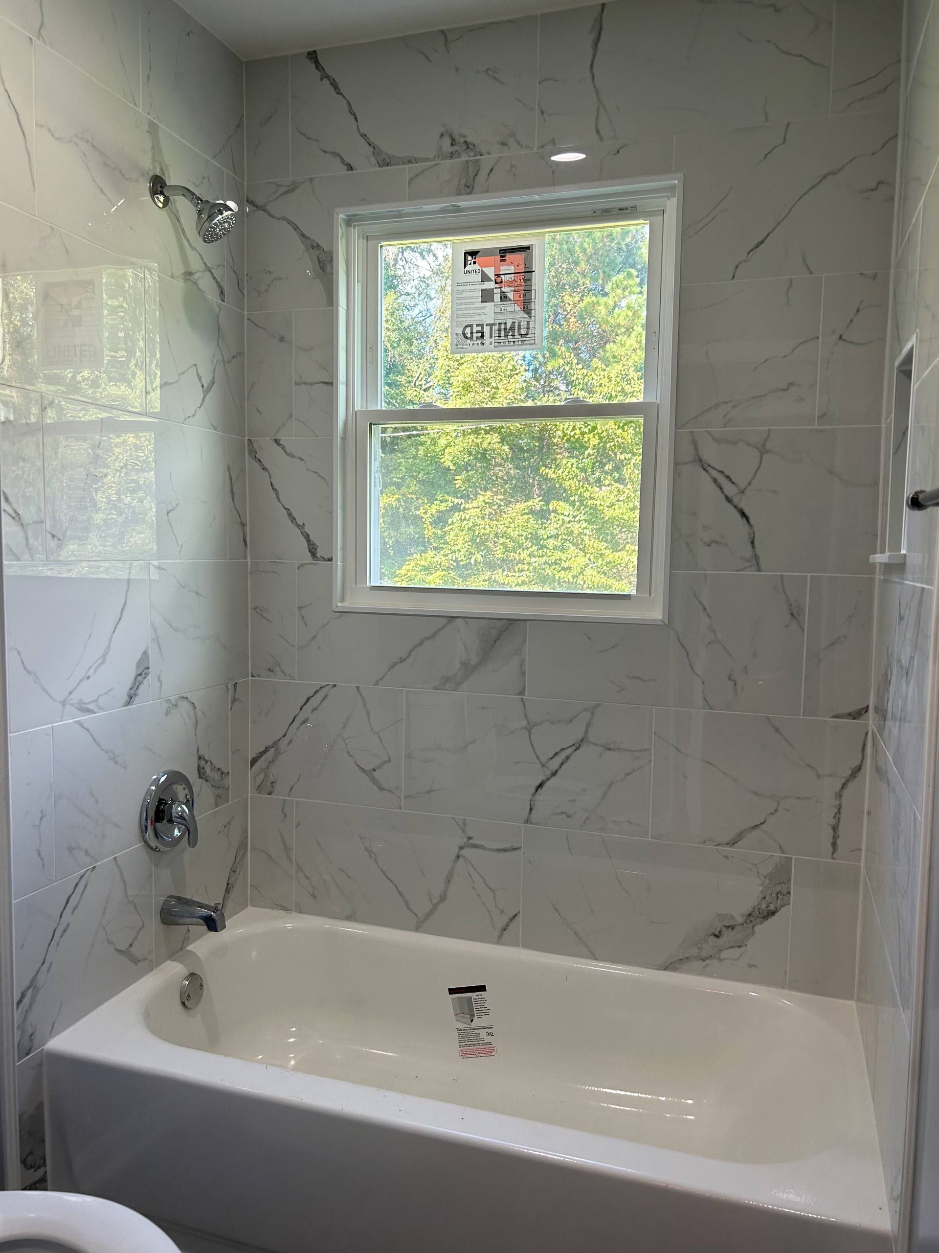 White marble-tiled bathroom with a bathtub and window above it.