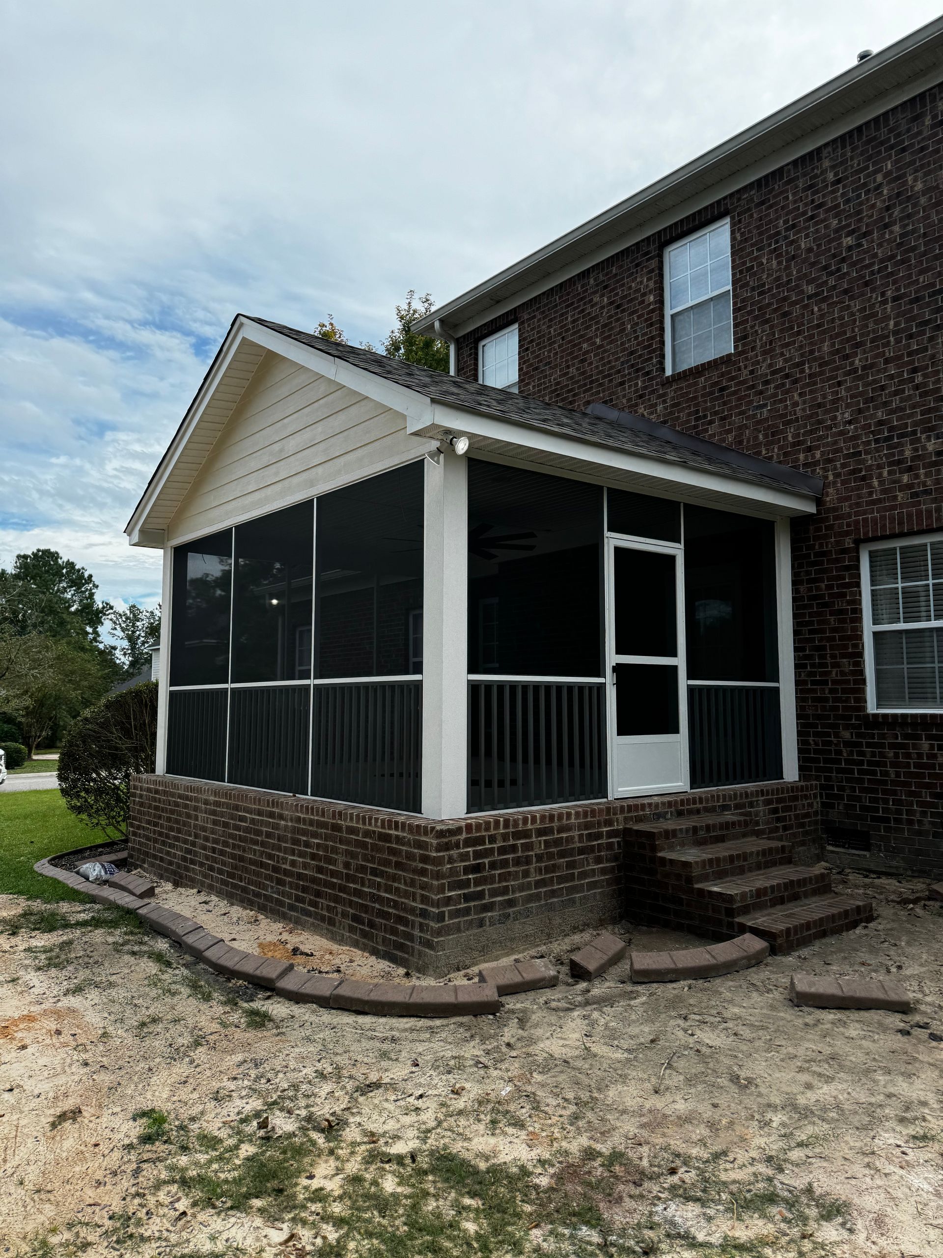 Screened front porch on a brick house with white trim and steps, set on a gravel yard.