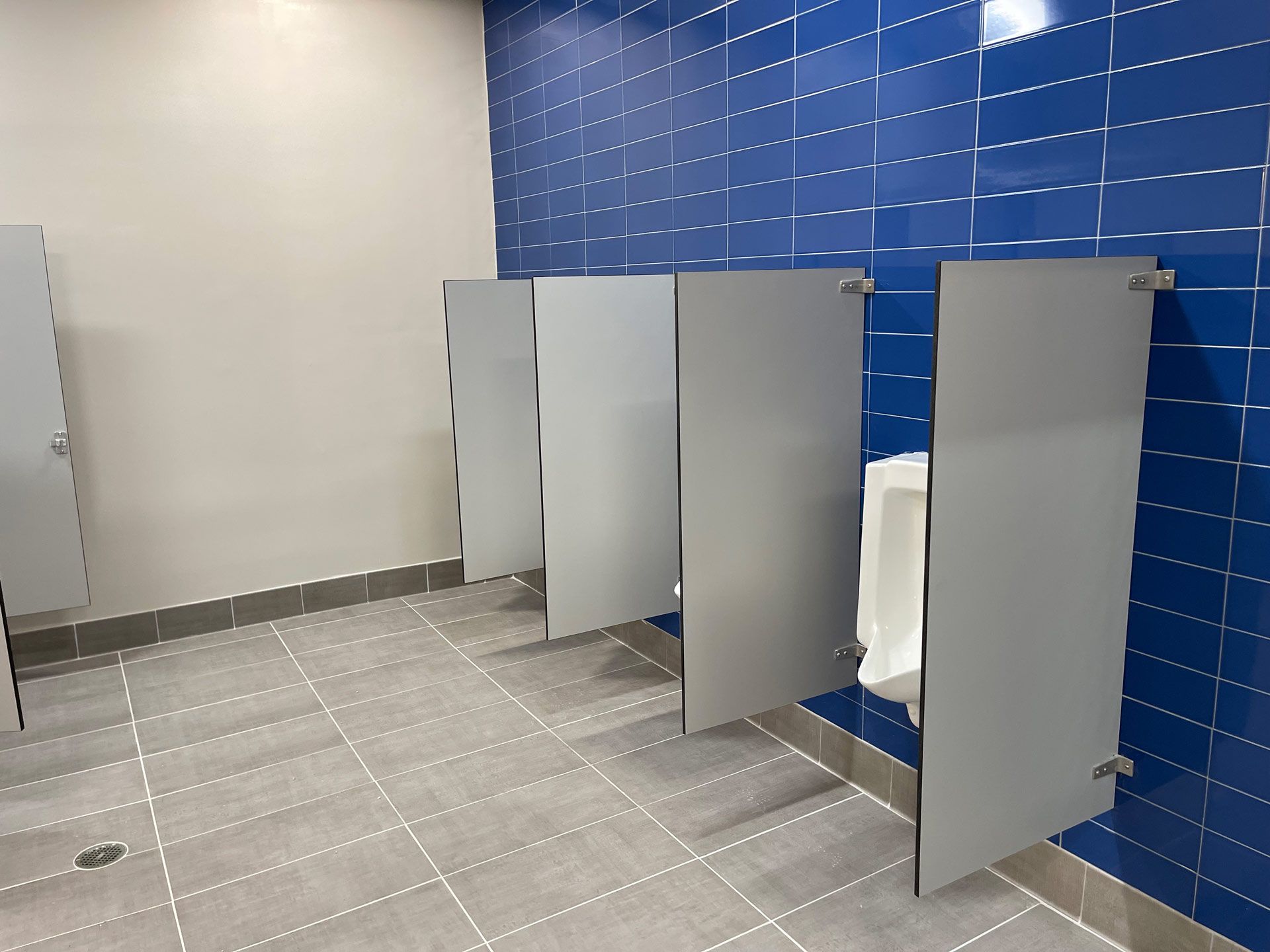 Public restroom with gray stall doors, tiled floor, and blue tiled wall panels.