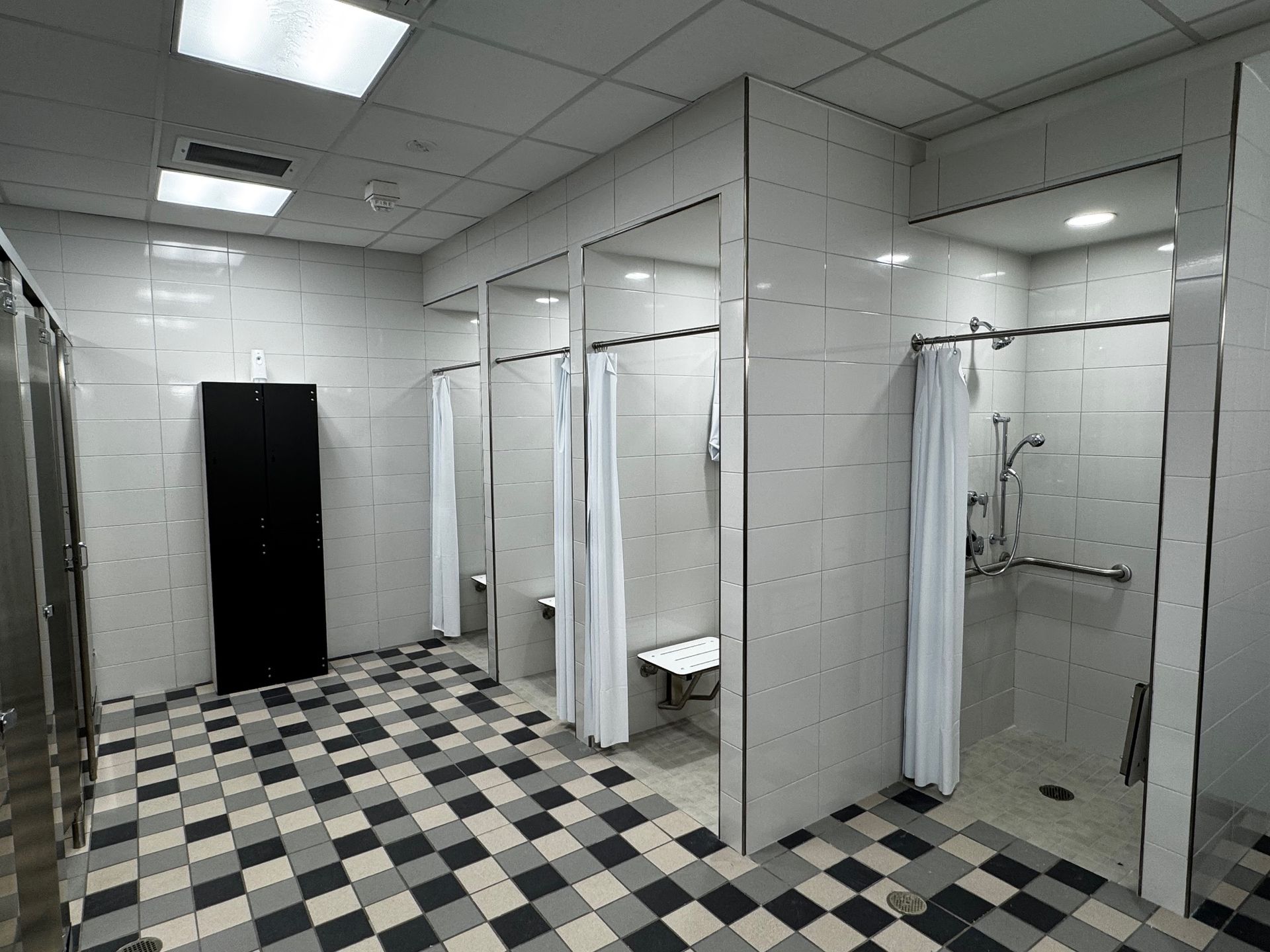 Public restroom with checkered floor, white stalls, mirrors, sinks, and a black privacy door