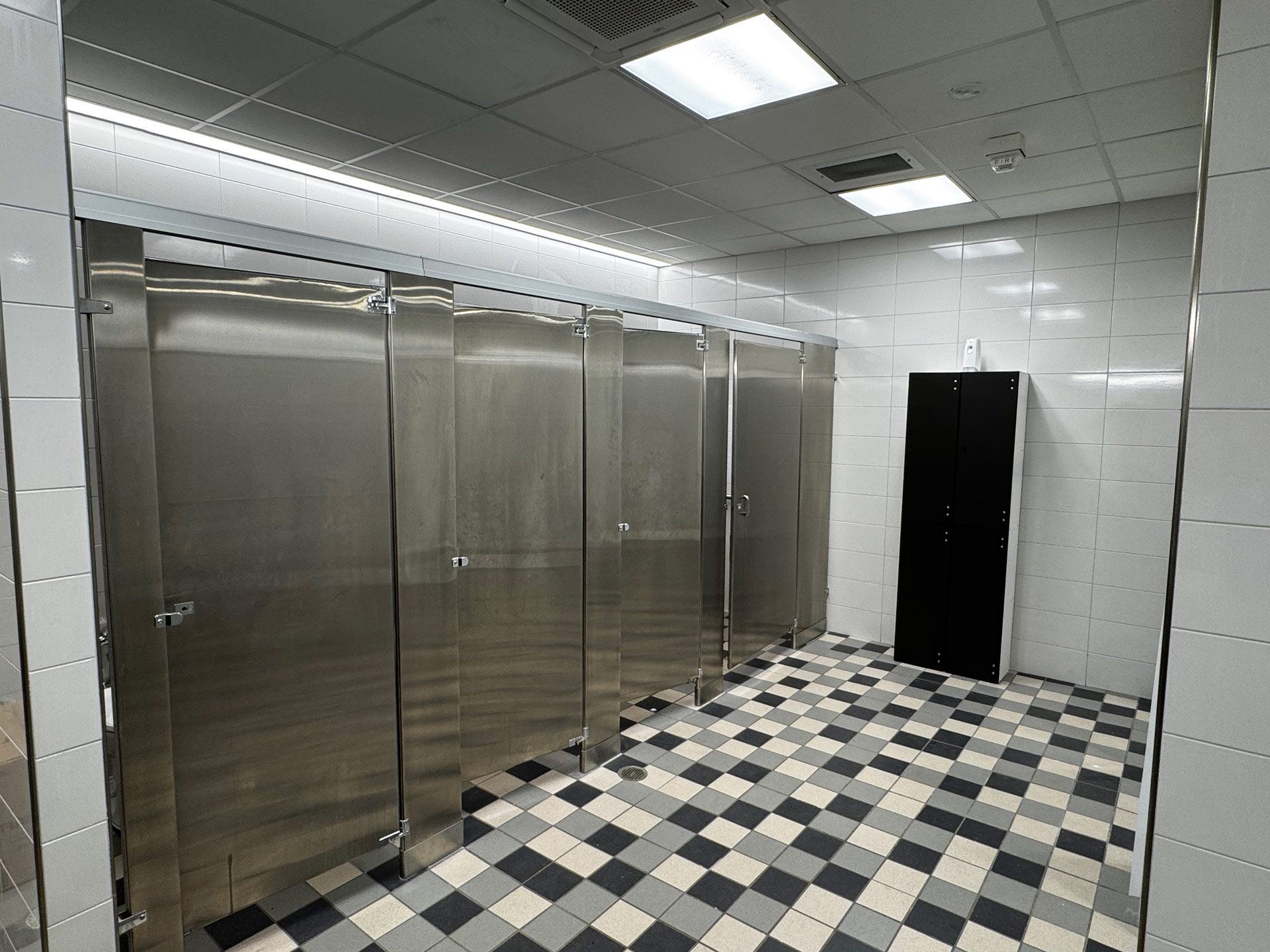 Stainless steel restroom stalls with black-and-white checkered floor and an open doorway.