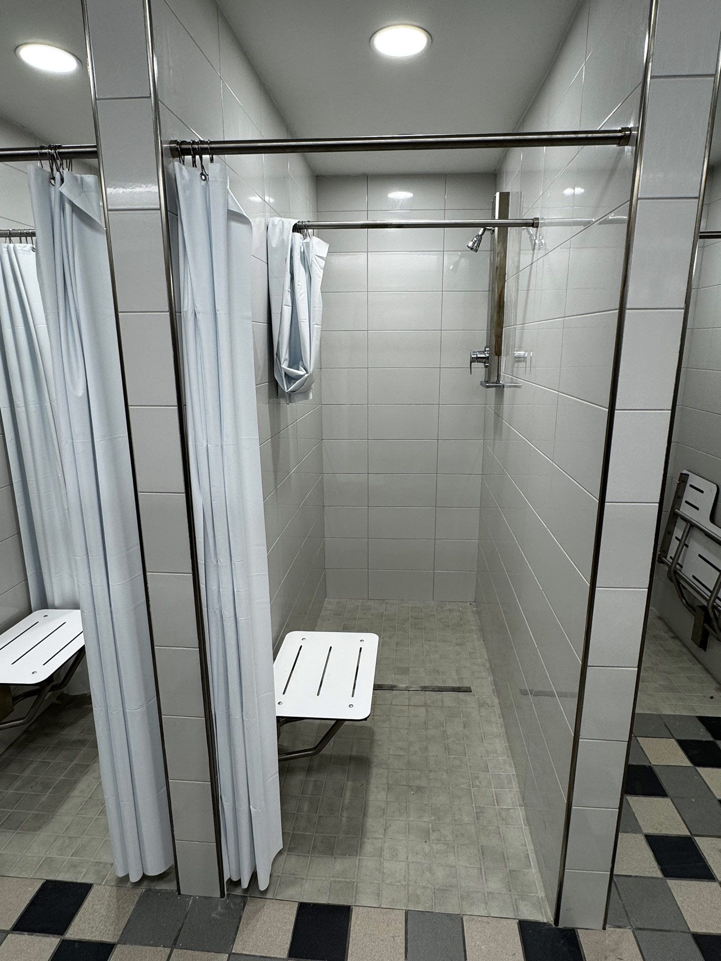 Accessible shower stall with curtains, grab bars, and fold-down seat in a tiled restroom
