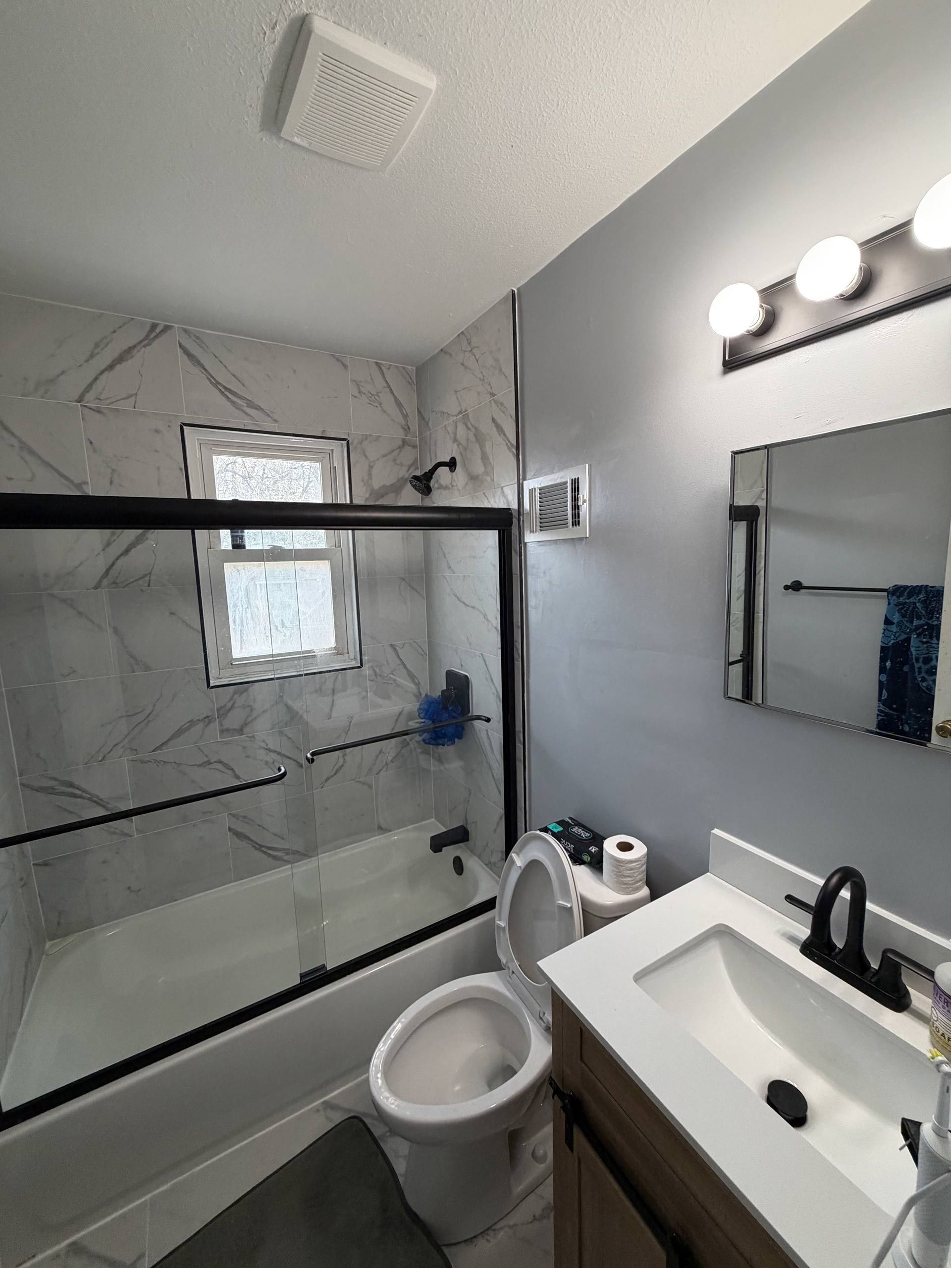 Small bathroom with glass shower, toilet, sink, mirror, and vanity lights.