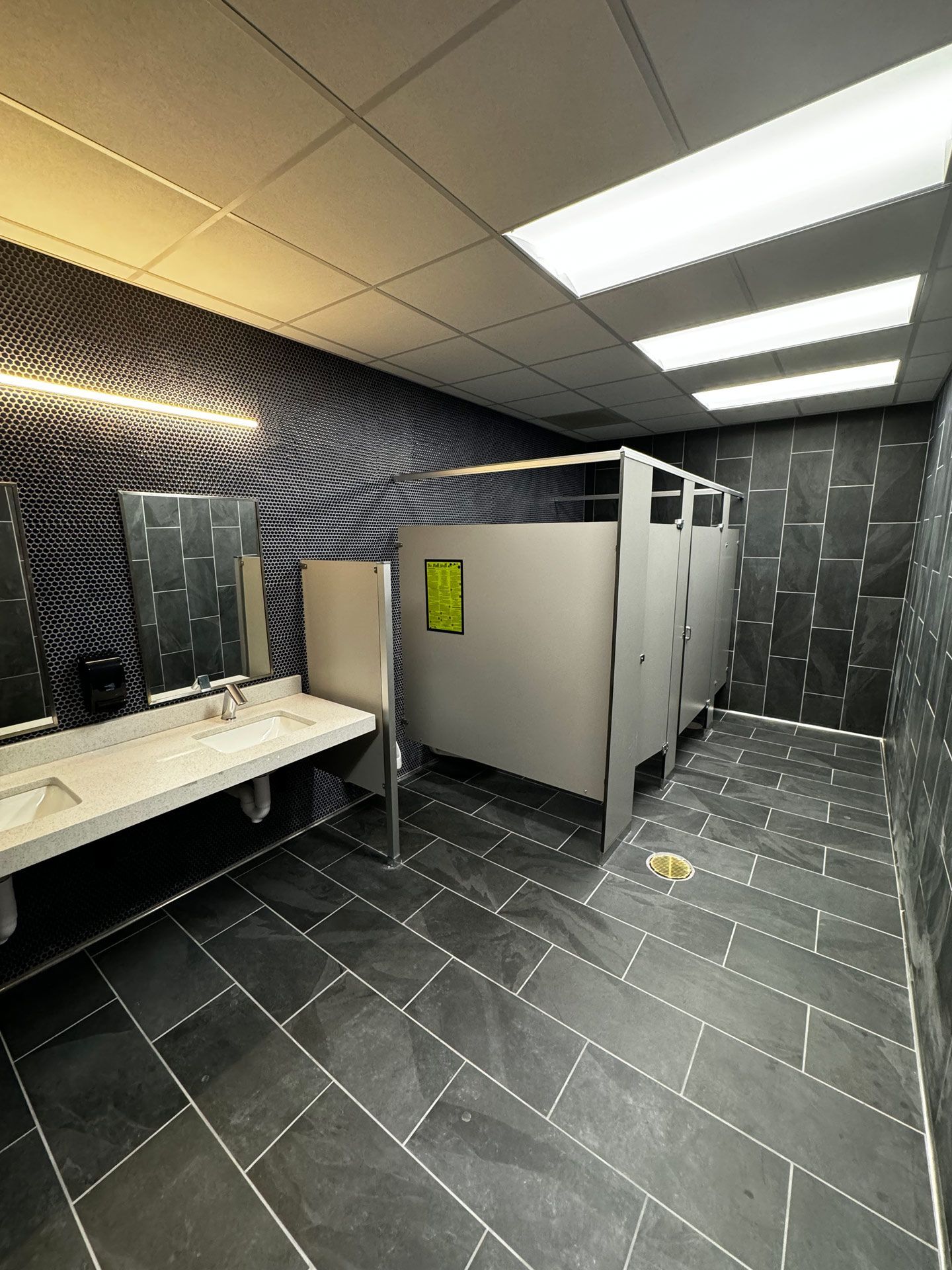 Public restroom with tiled stalls, sinks, mirrors, and dark patterned walls