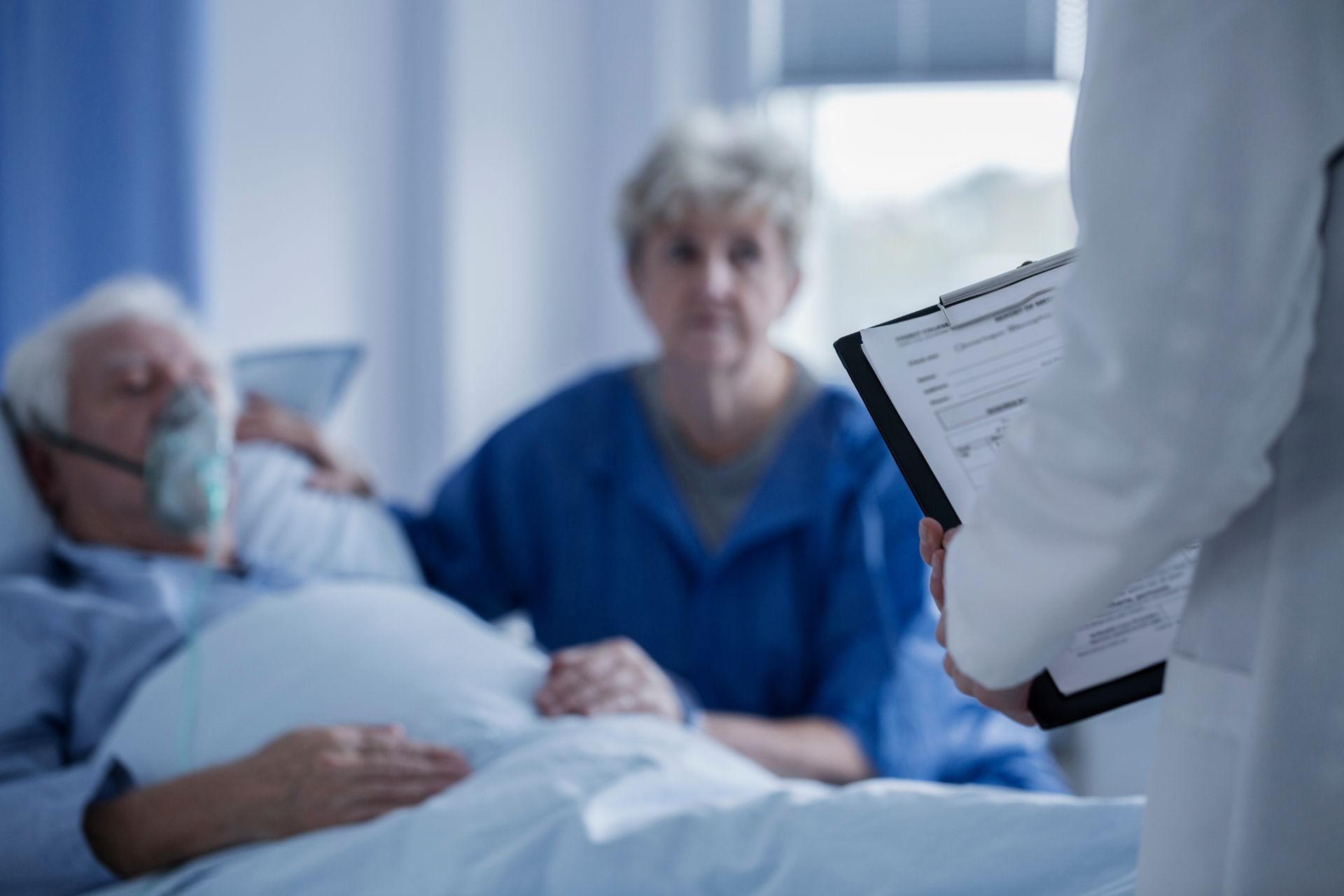 doctor consults with wife and sick husband beside hospital bed