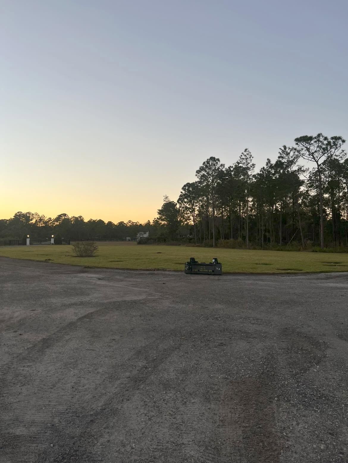 Gravel lot at sunset with a parked go-kart and trees in the distance.