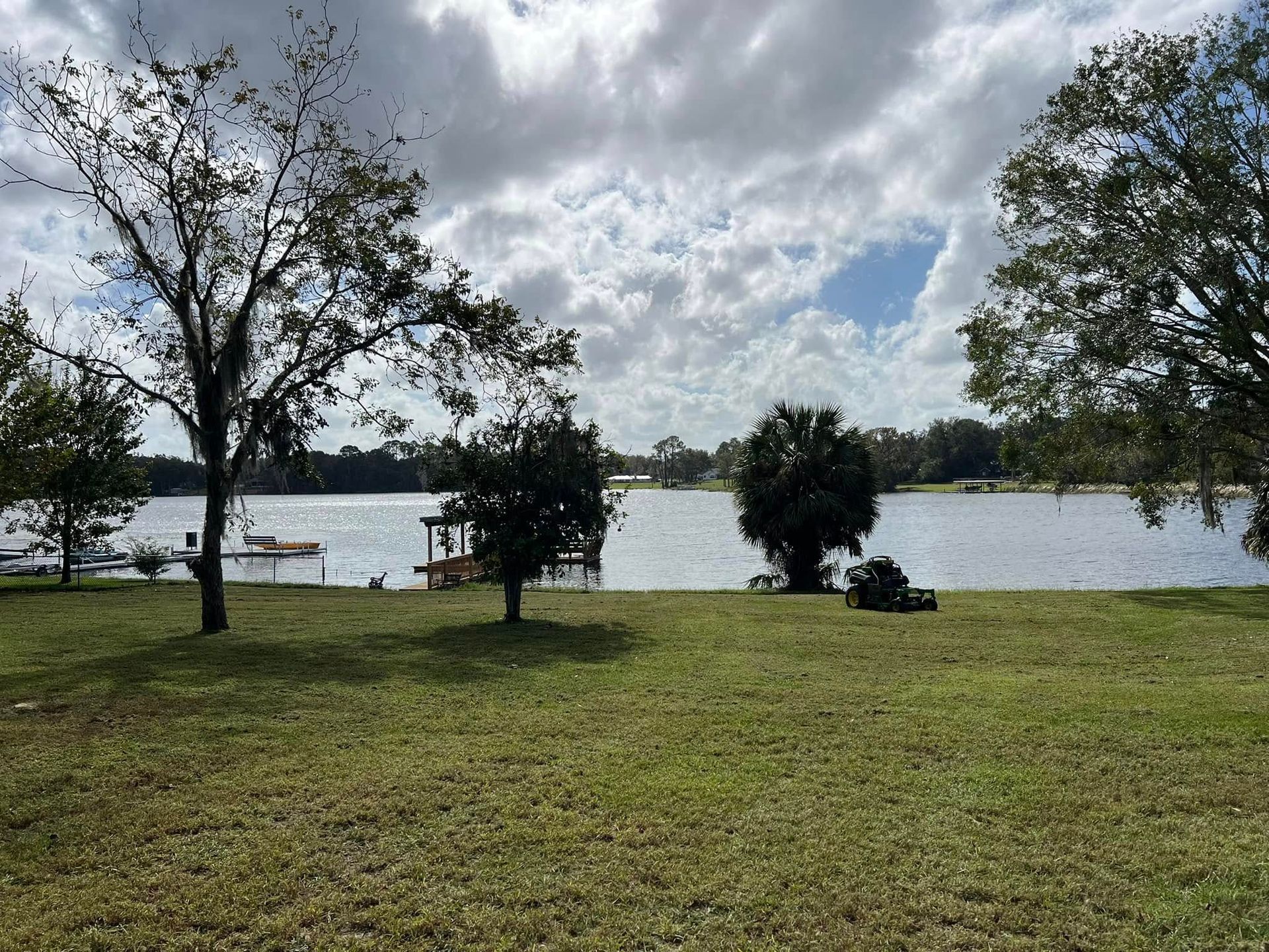 Grassy lakeside park with trees, cloudy sky, and water in the background