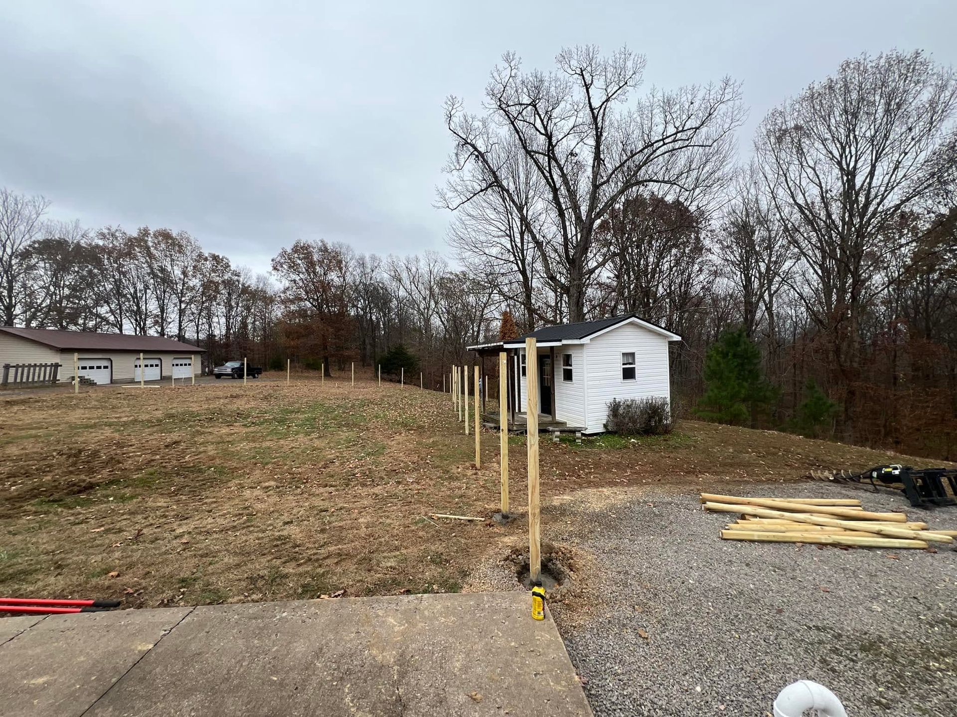 Gravel lot with yellow posts, a small white shed, and bare trees under a cloudy sky