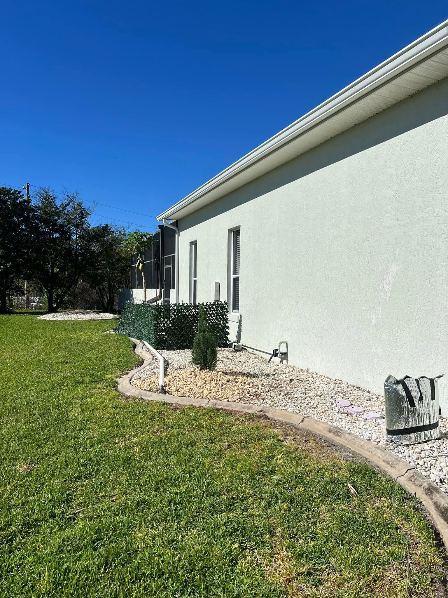White stucco house exterior with a green lawn, shrubs, and a gravel border under a blue sky