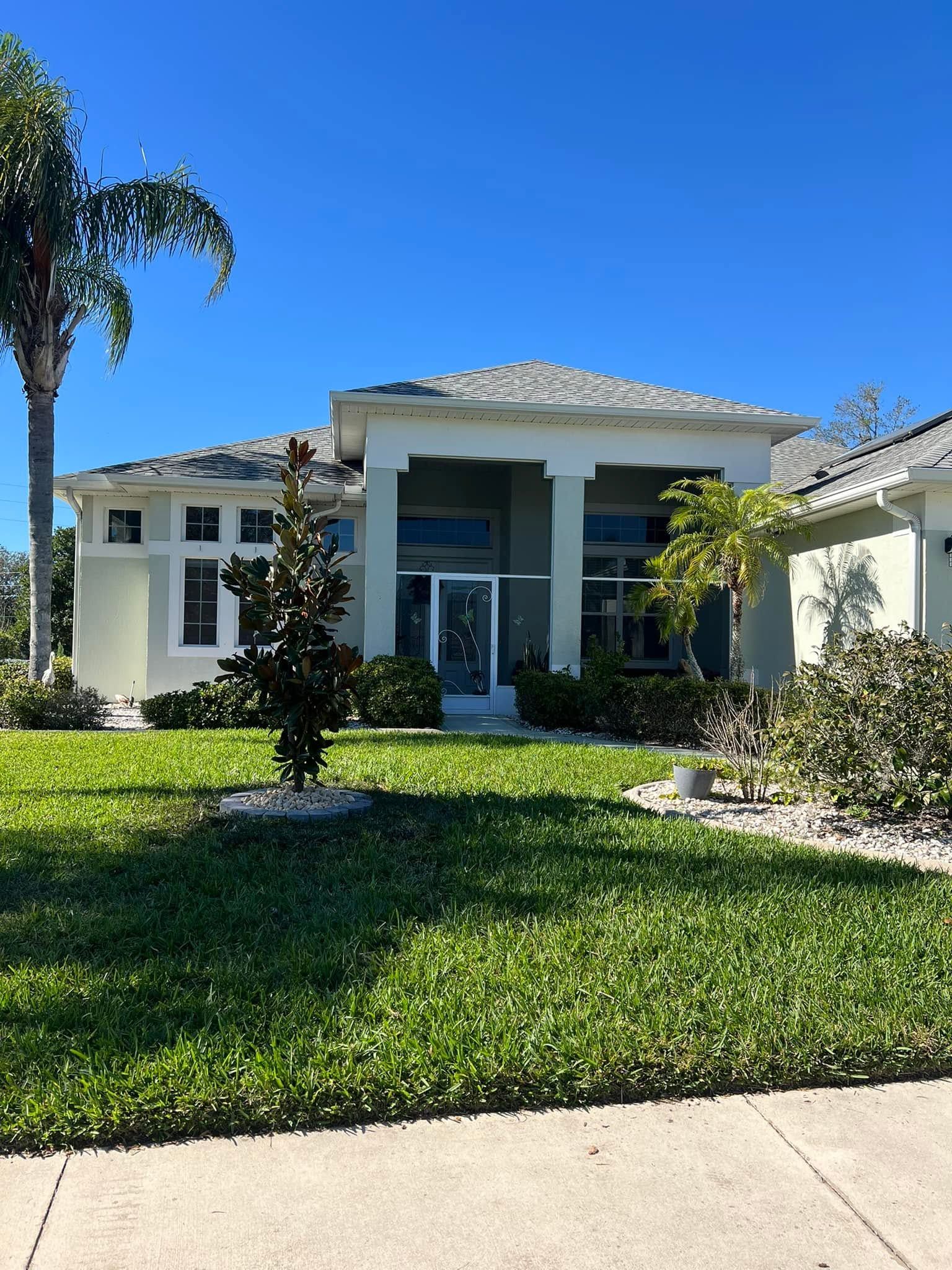 Single-story white house with a columned front porch, green lawn, and palm tree under a clear blue sky