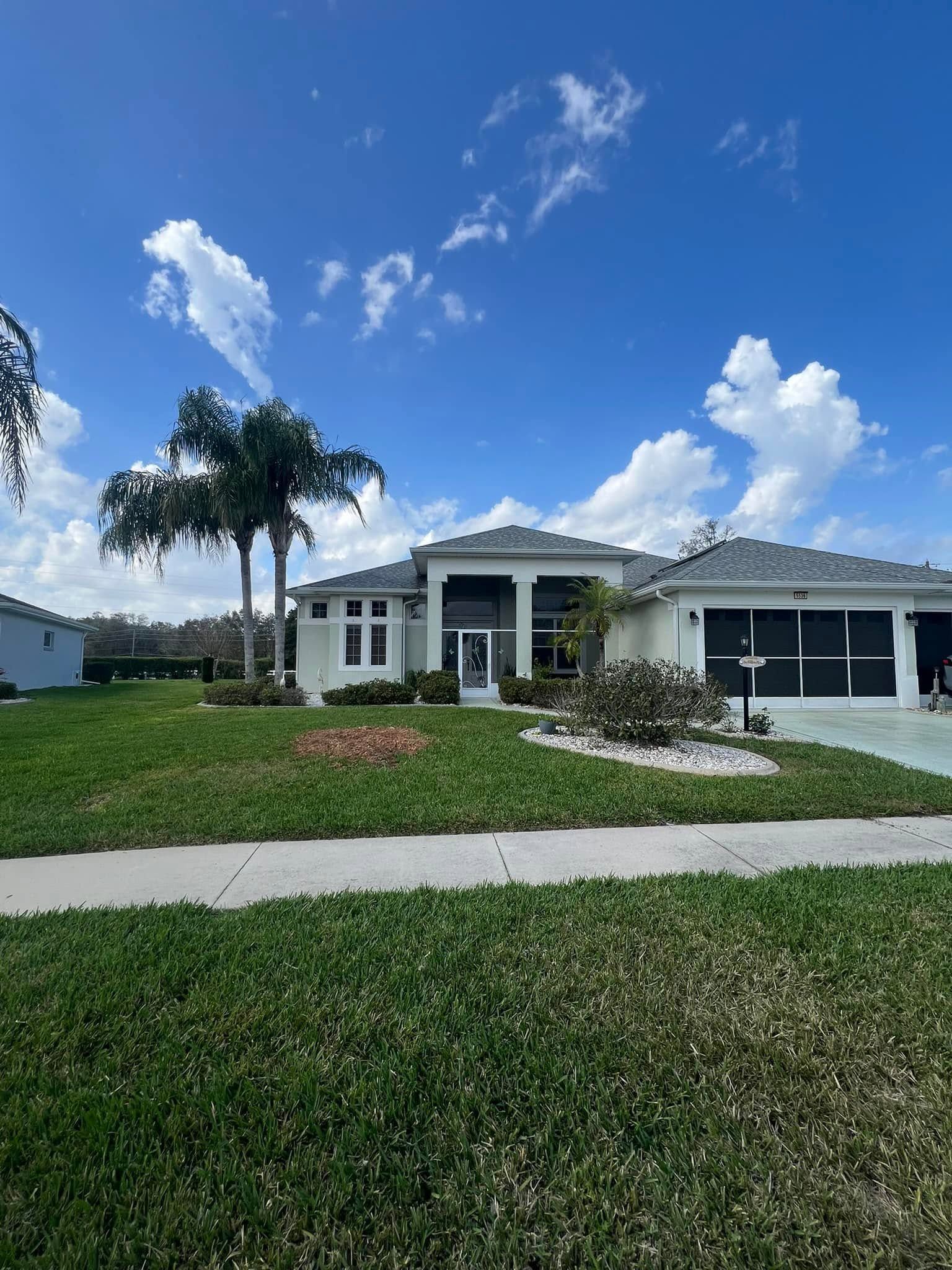 Single-story suburban house with palm trees, a manicured lawn, and a bright blue sky.