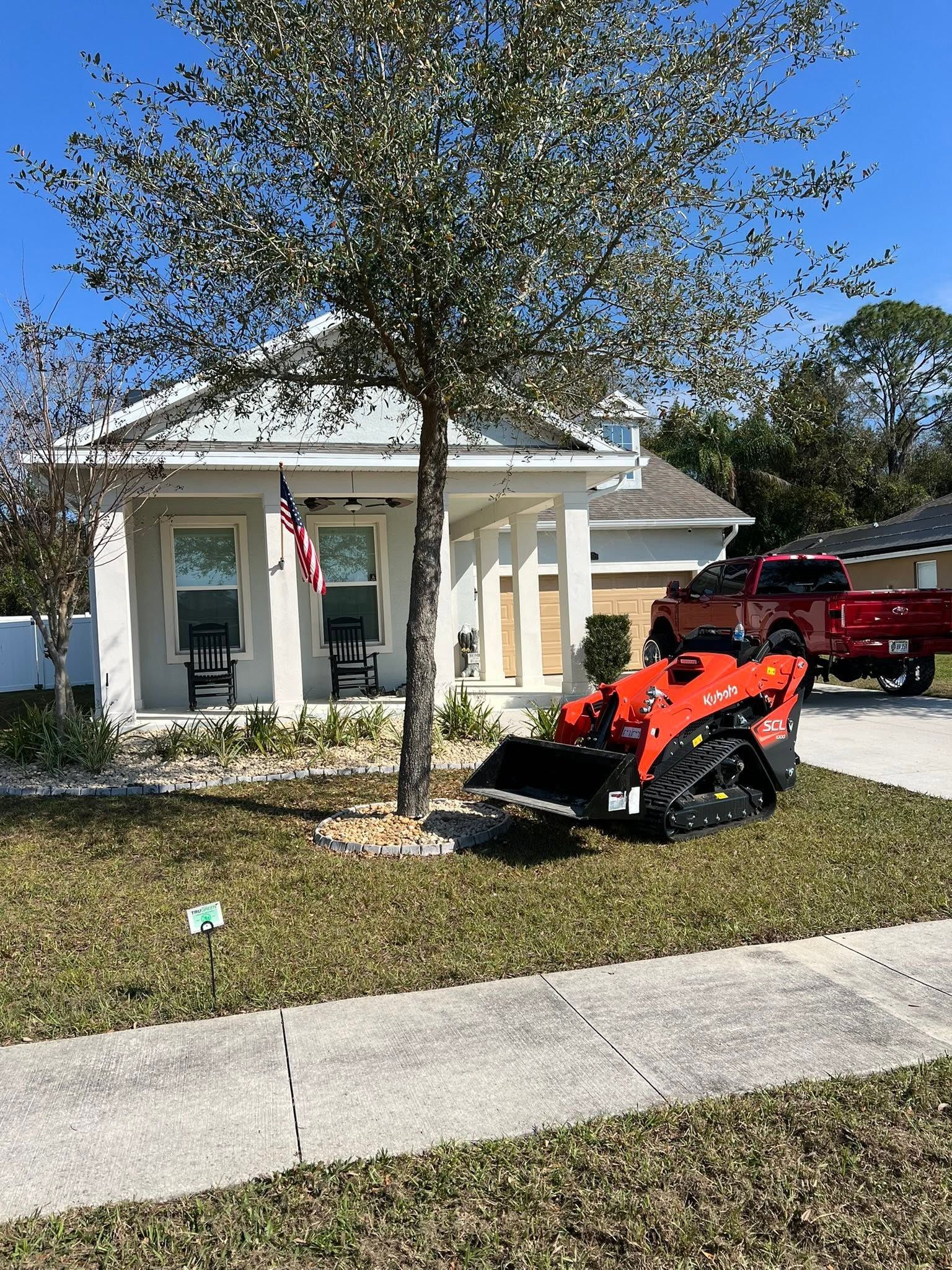 Suburban house with a tree in front, an orange snowblower on the lawn, and a red truck in the driveway