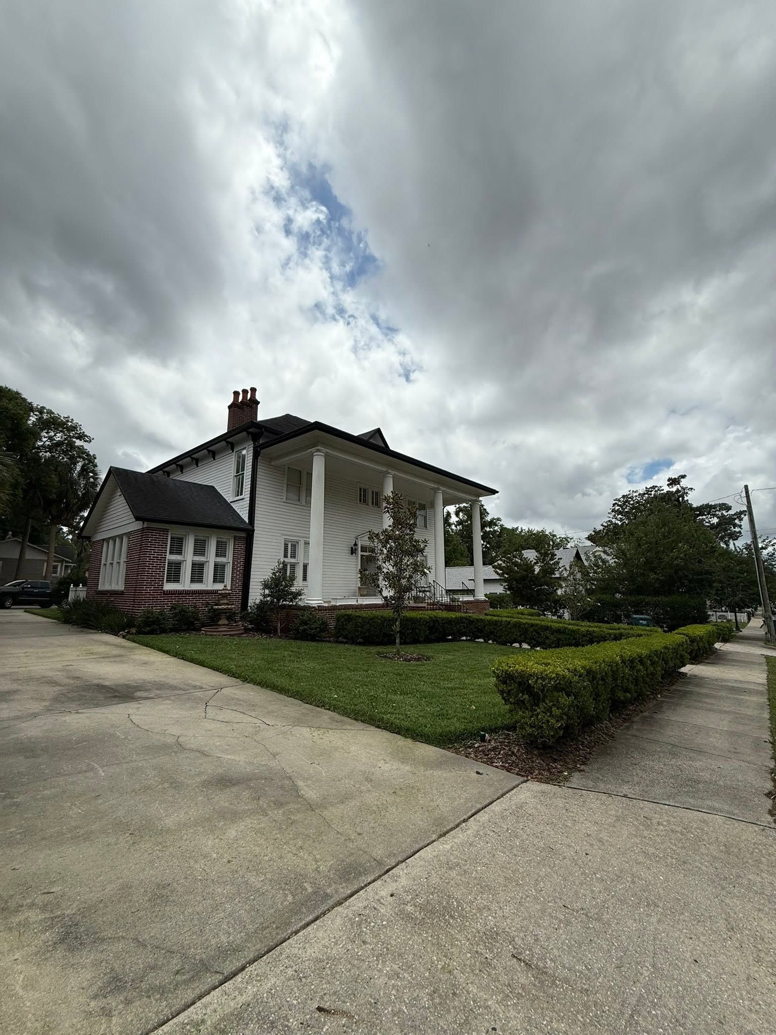 Large white house with columns on a cloudy day, viewed from a sloped driveway with a landscaped yard.