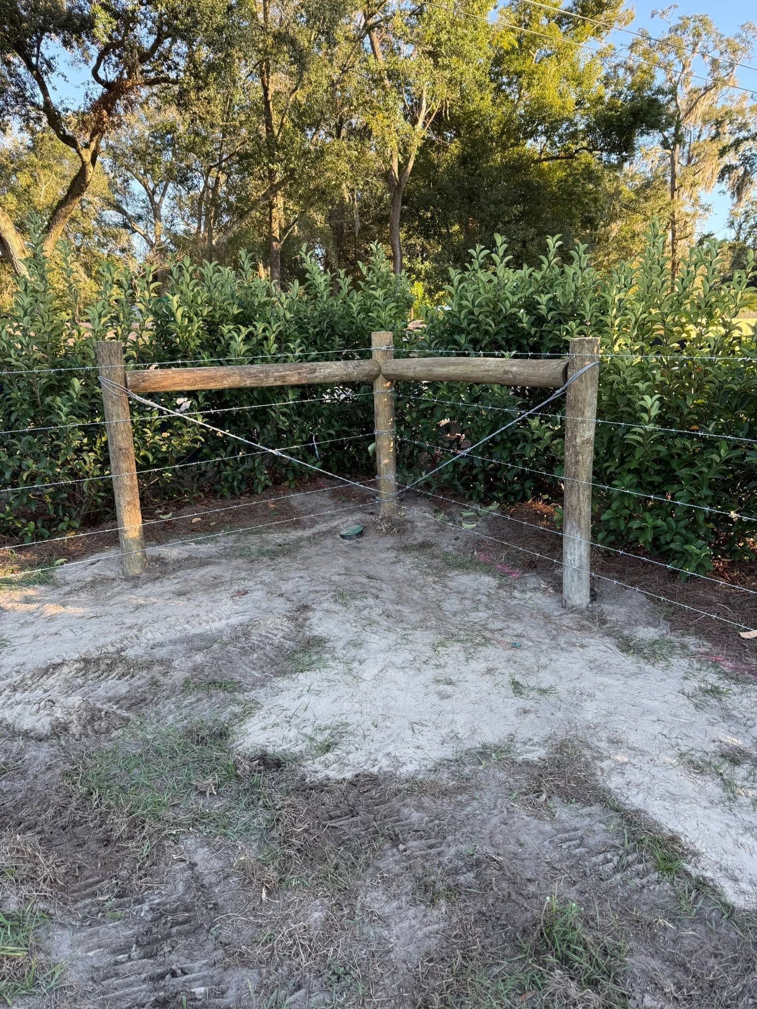 Wooden barrier blocking a dirt clearing, with trees and dense greenery in the background.