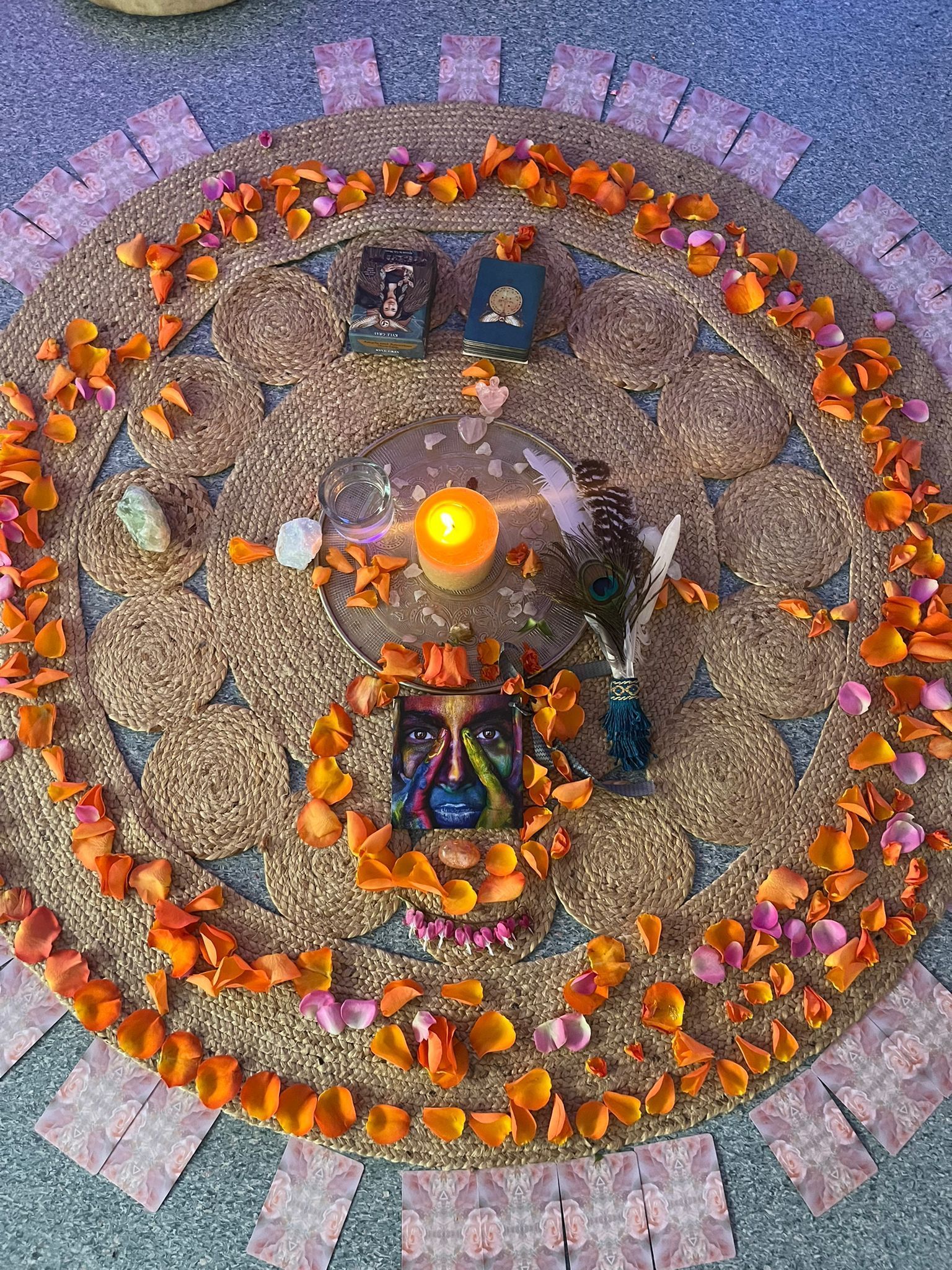 Rond altaar met kaars, tarotkaarten, bloemblaadjes, kristallen en pauwenveer.