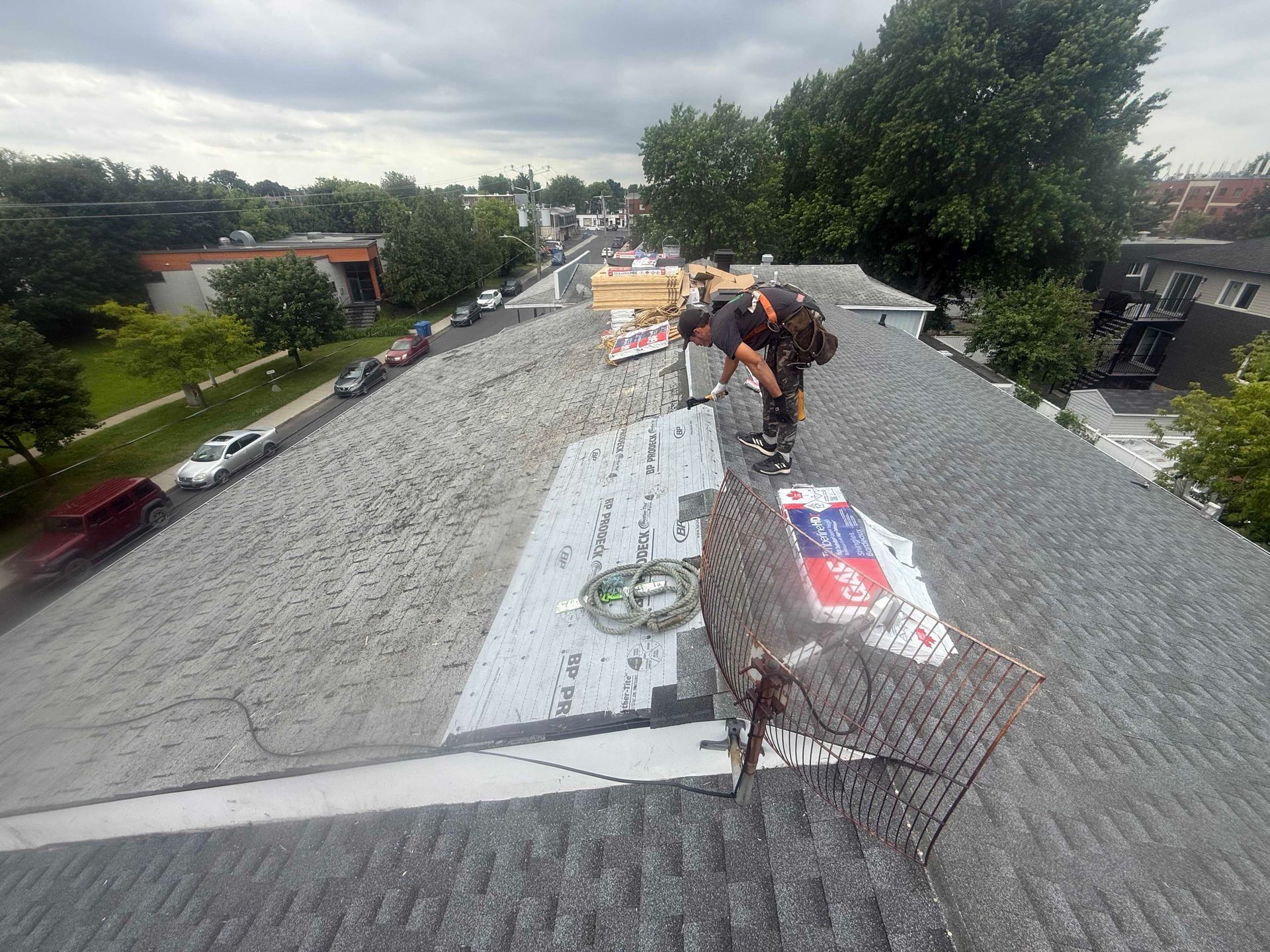Des couvreurs travaillent sur un toit en bardeaux gris dans une zone résidentielle.