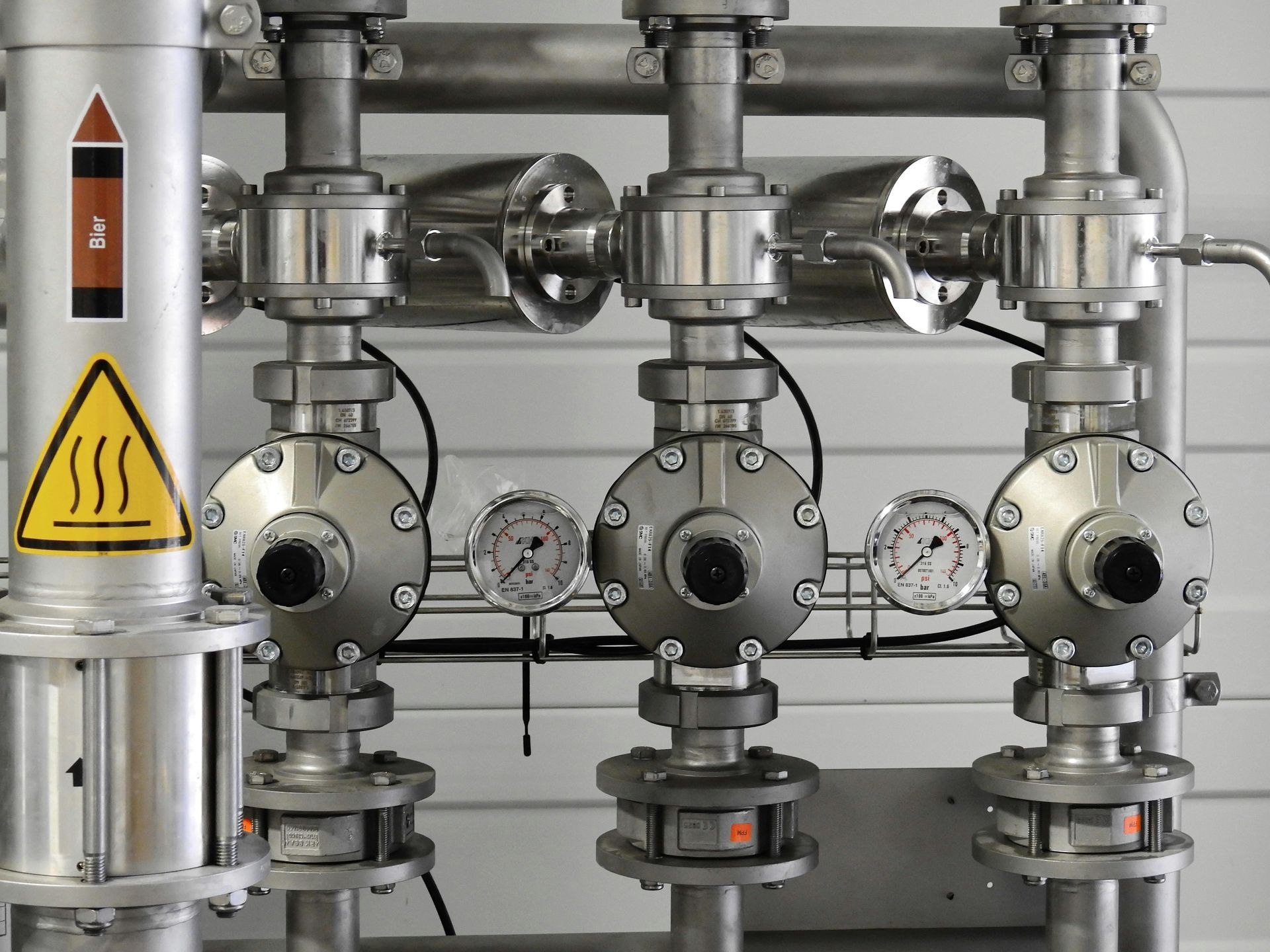 Industrial pipes with valves, gauges, and a heat hazard warning.