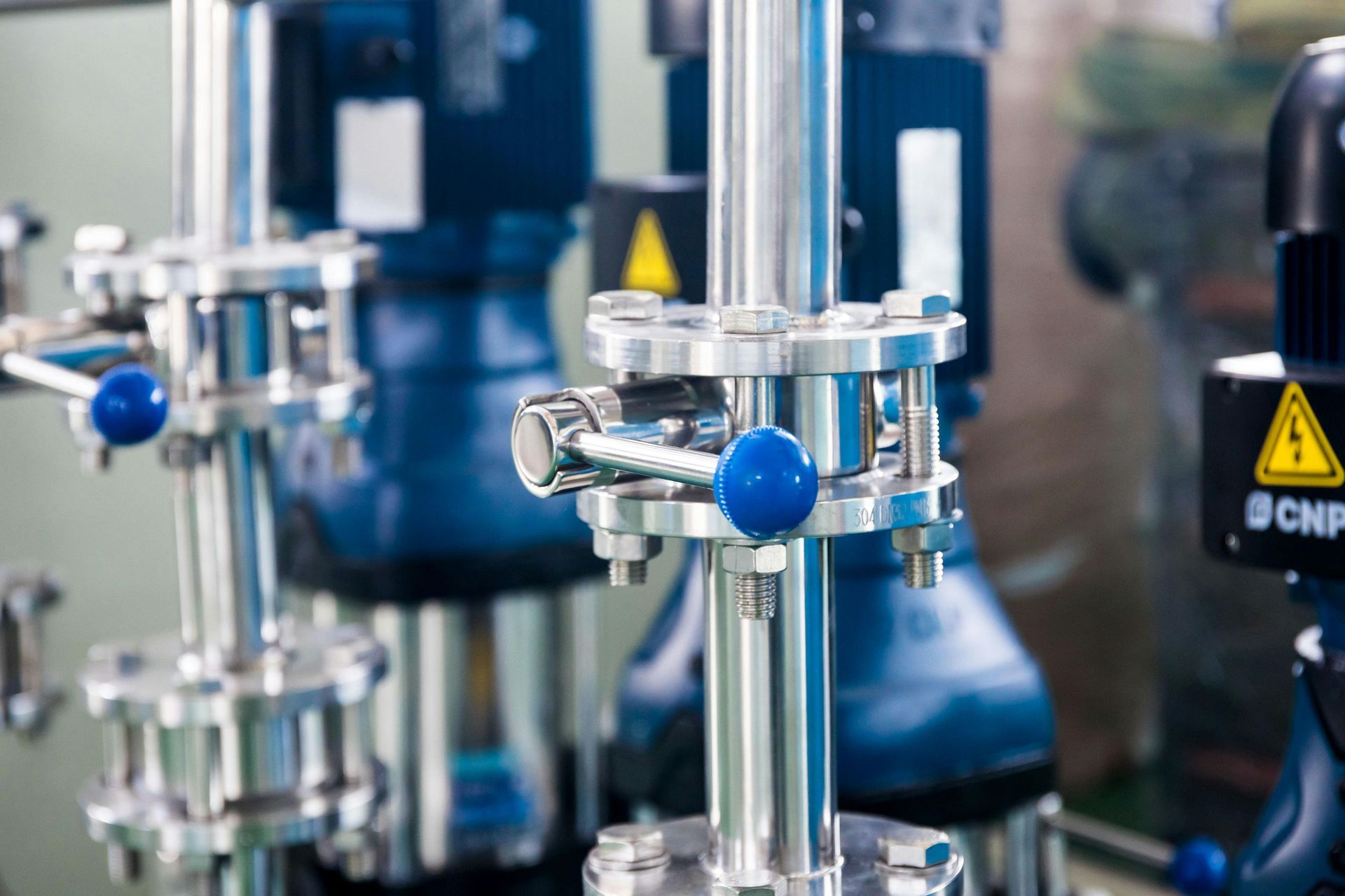 Industrial machinery with blue motors and shiny metal pipes, featuring blue valve handles.