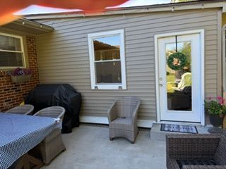 Patio with wicker chairs, table, grill, and a door decorated with a wreath