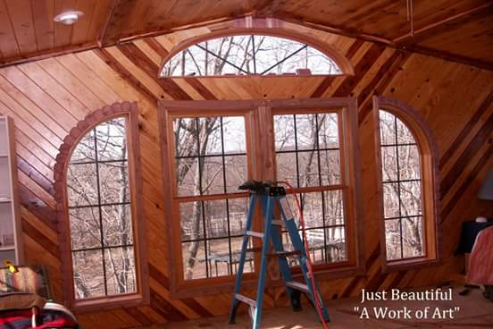 Wood-paneled sunroom with arched windows and a blue ladder in front of a large window.