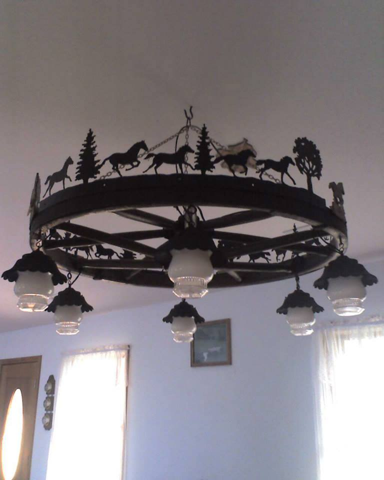 Rustic metal chandelier with hanging glass lamps and horse silhouettes on a ceiling in a room
