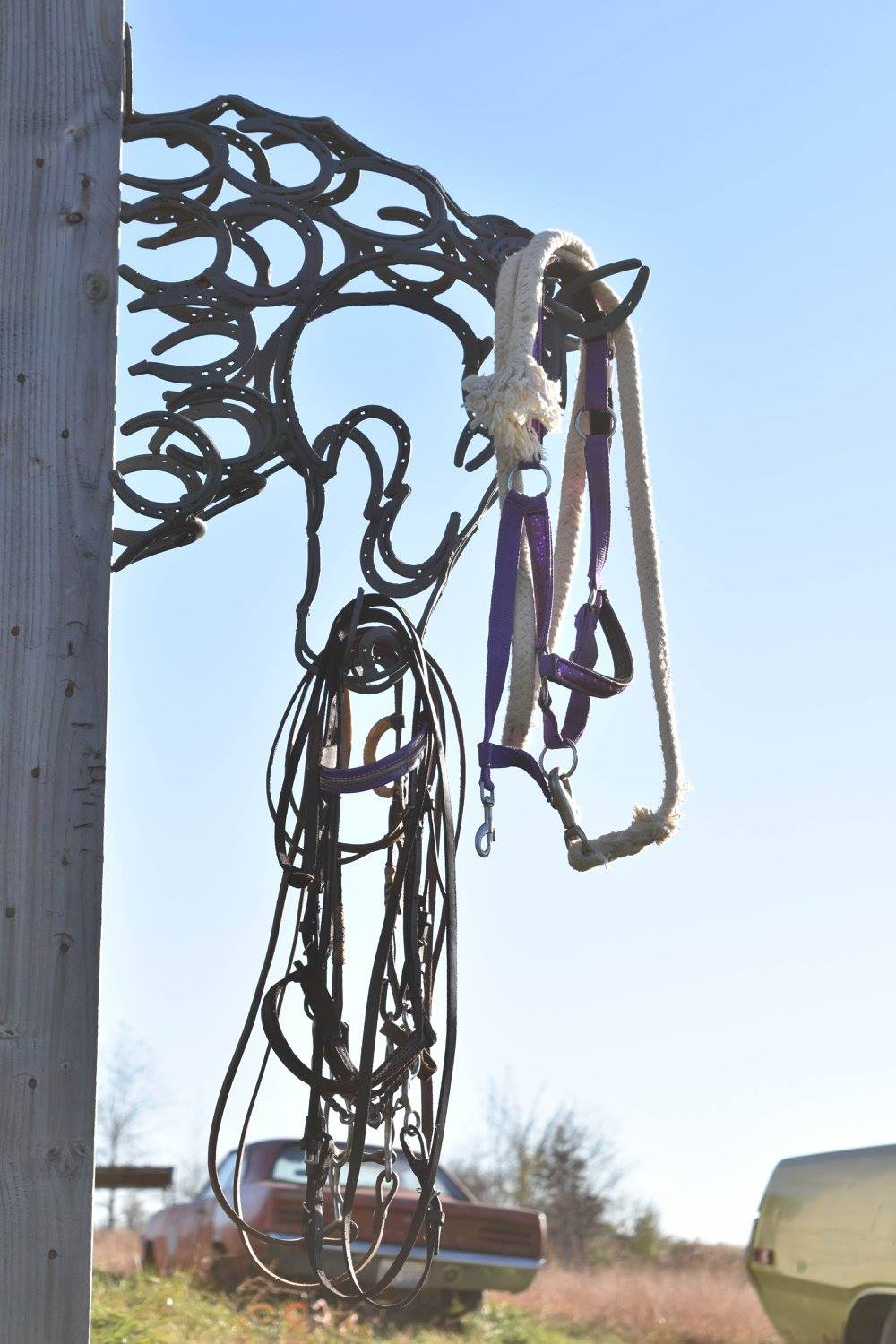 Rusty hanging metal sculpture resembling a horse head outdoors against a blue sky